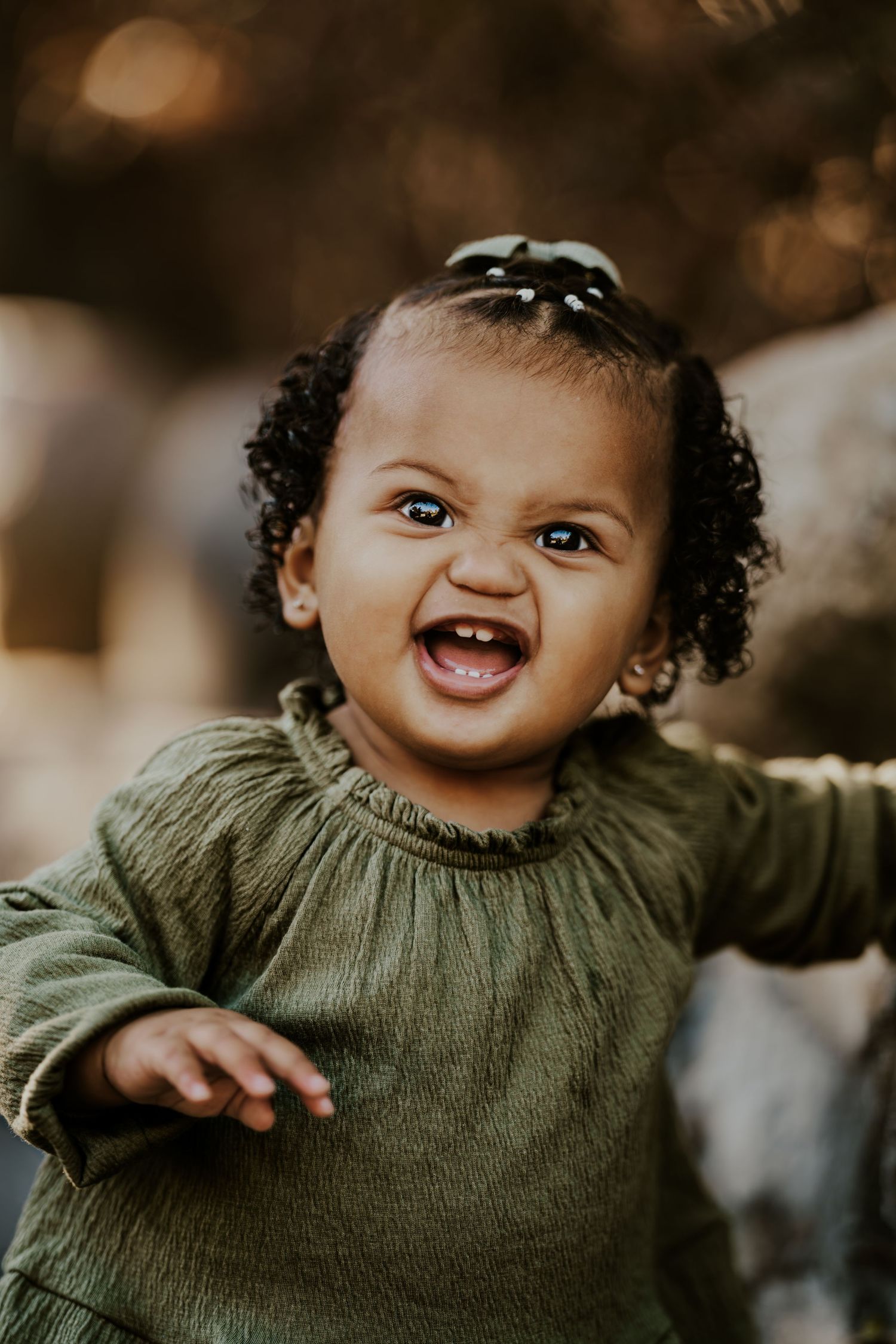 A joyful baby in a green sweater smiles brightly at the camera.