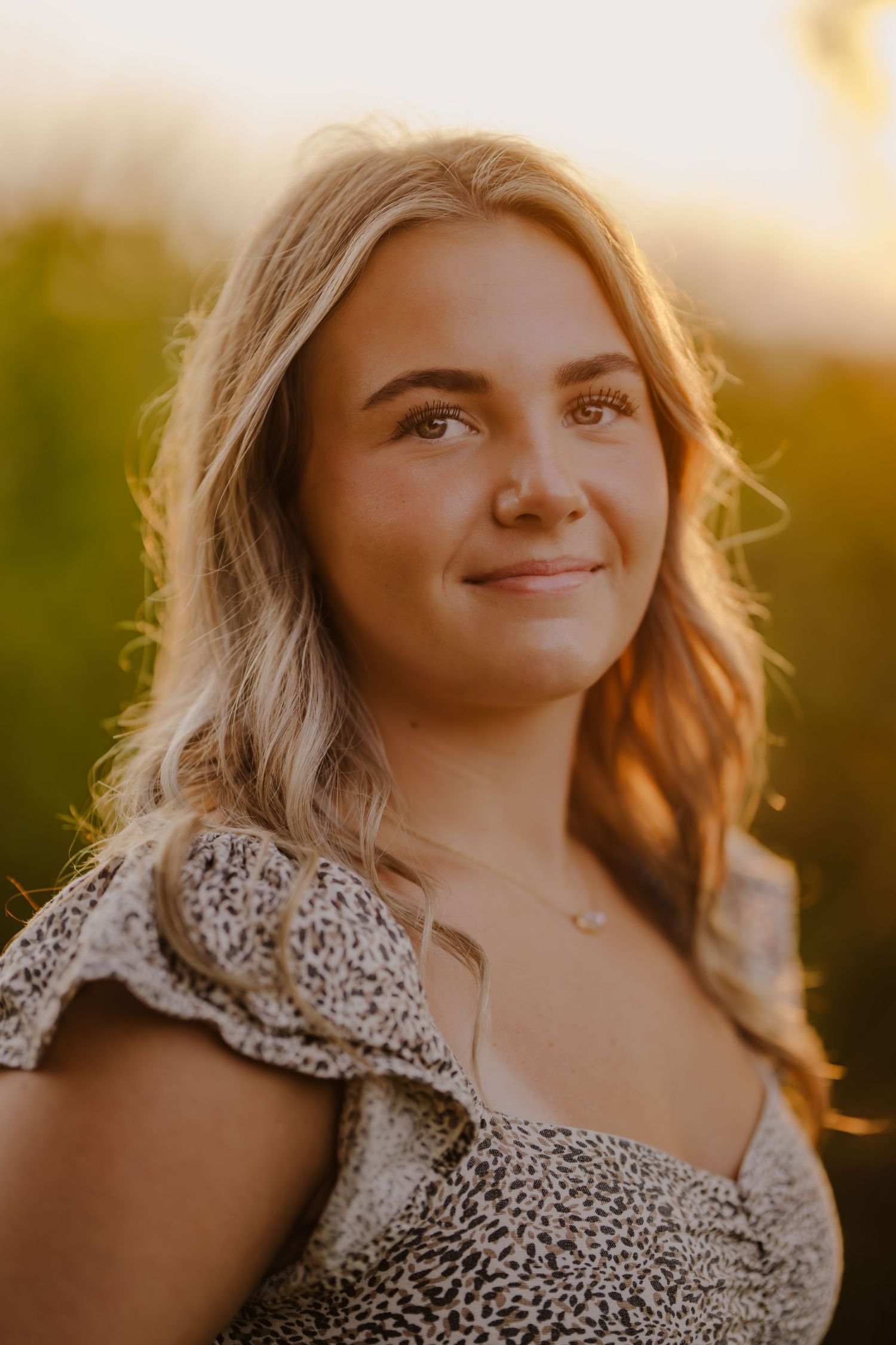 Portrait of woman in patterned dress backlit by golden sunset.