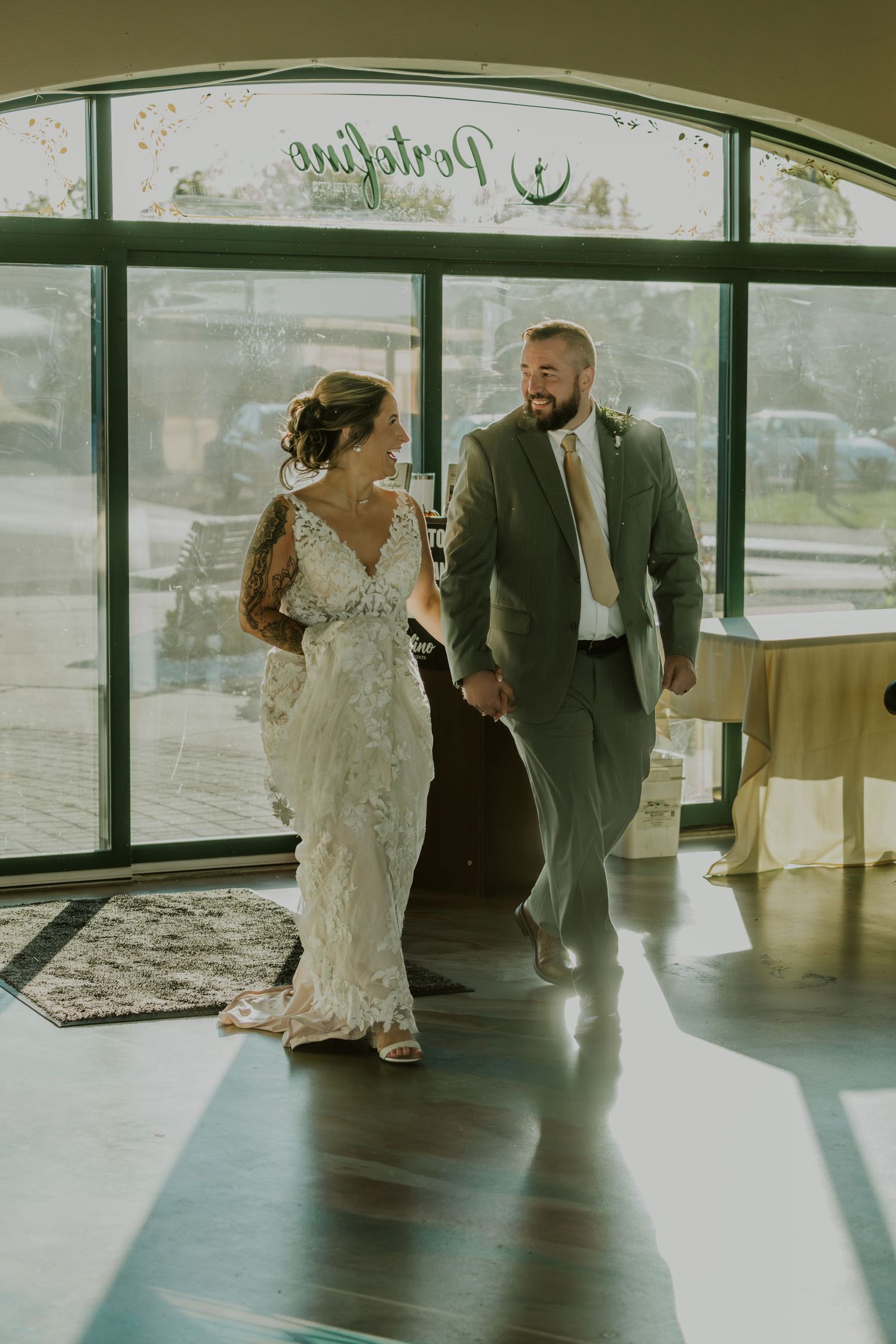A couple shares a romantic dance moment in a sunlit venue with large windows.