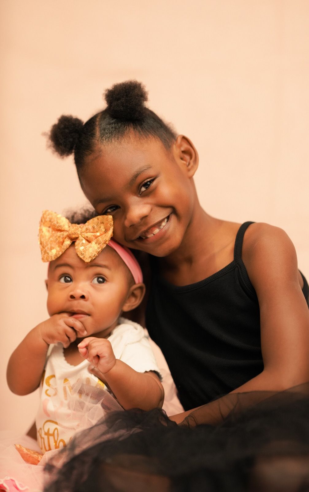 Studio portrait series showing tender moments of sisterly affection against peachy backdrop.