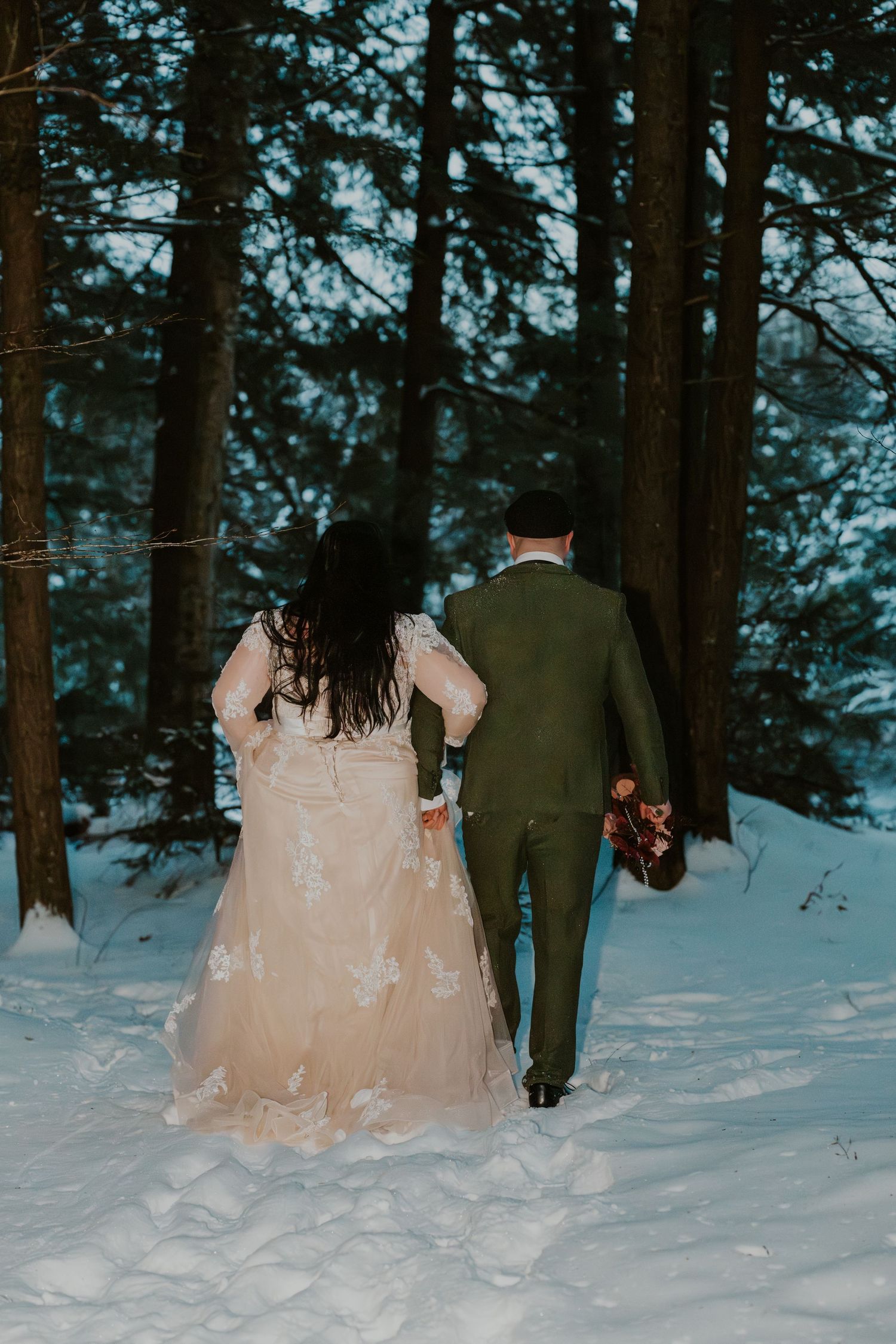 Wedding couple walking through snowy forest with flowing blush gown.