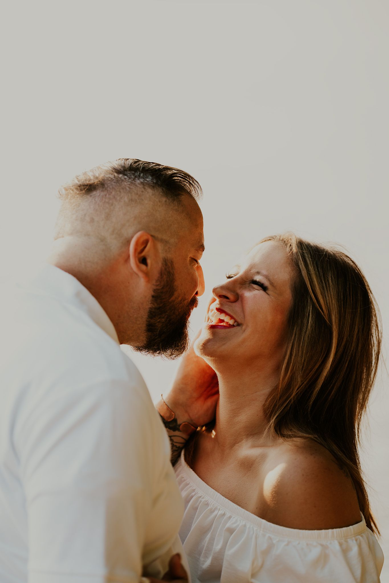 A joyful couple shares a candid laughing moment in natural light.