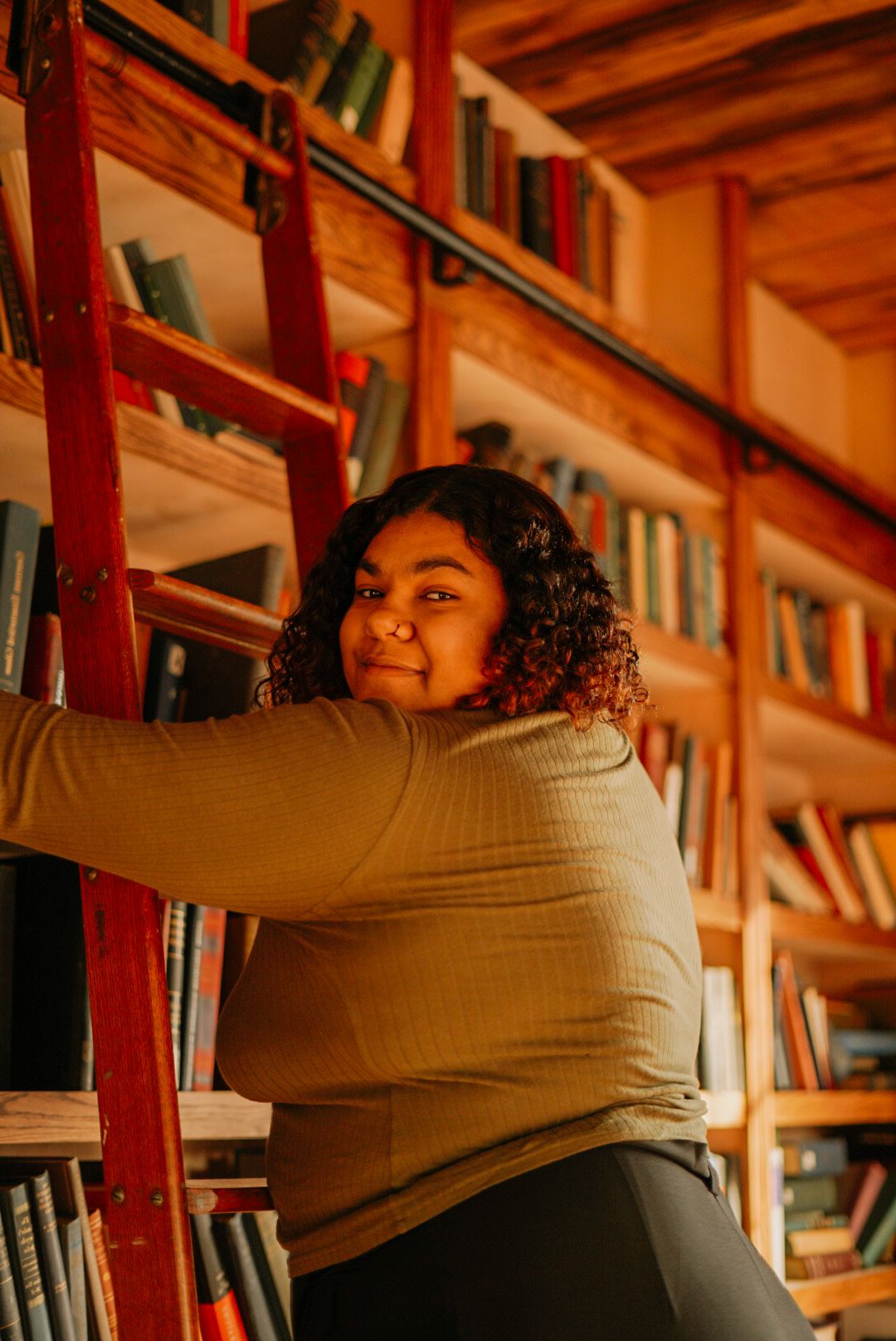 Person reaching for books on wooden library shelves in warm lighting.