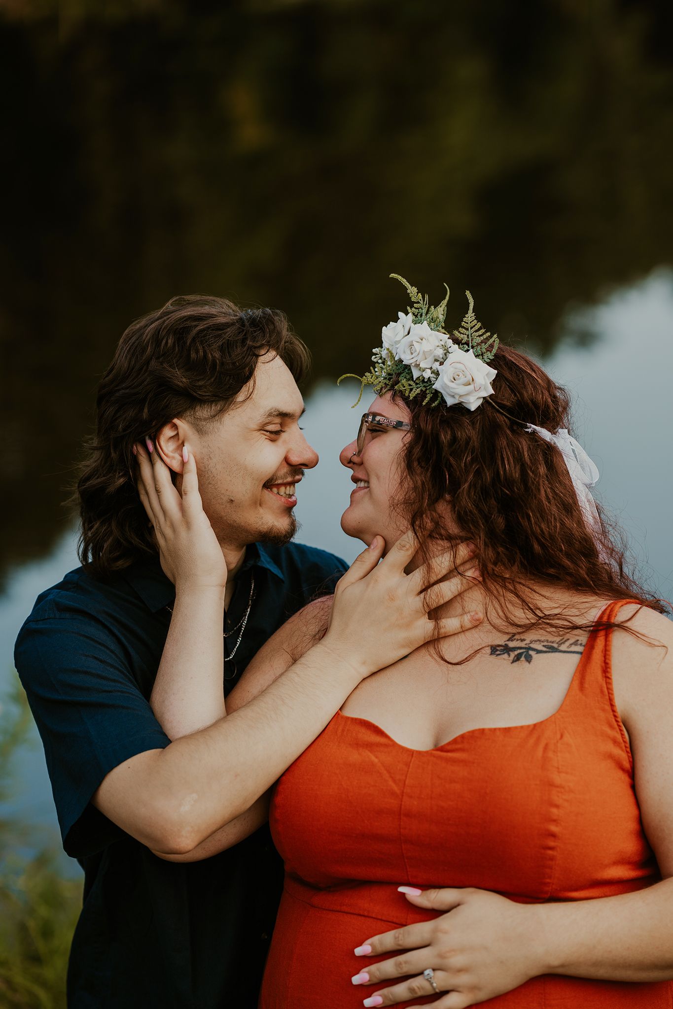 A romantic couple shares an intimate moment outdoors, with one wearing orange and a floral crown.
