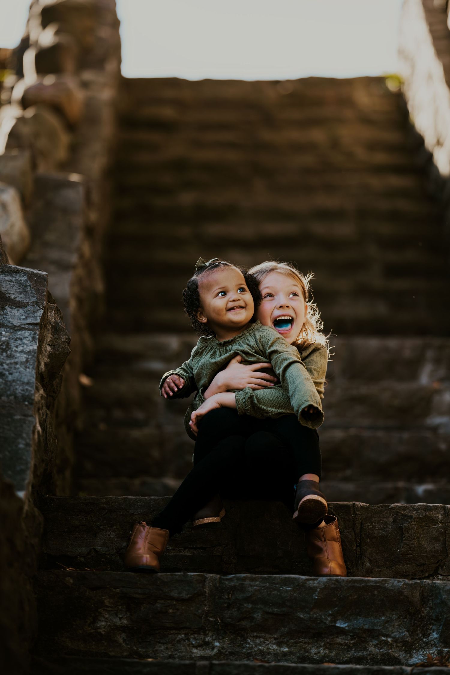 Two children share a heartwarming laugh while sitting on stone steps.