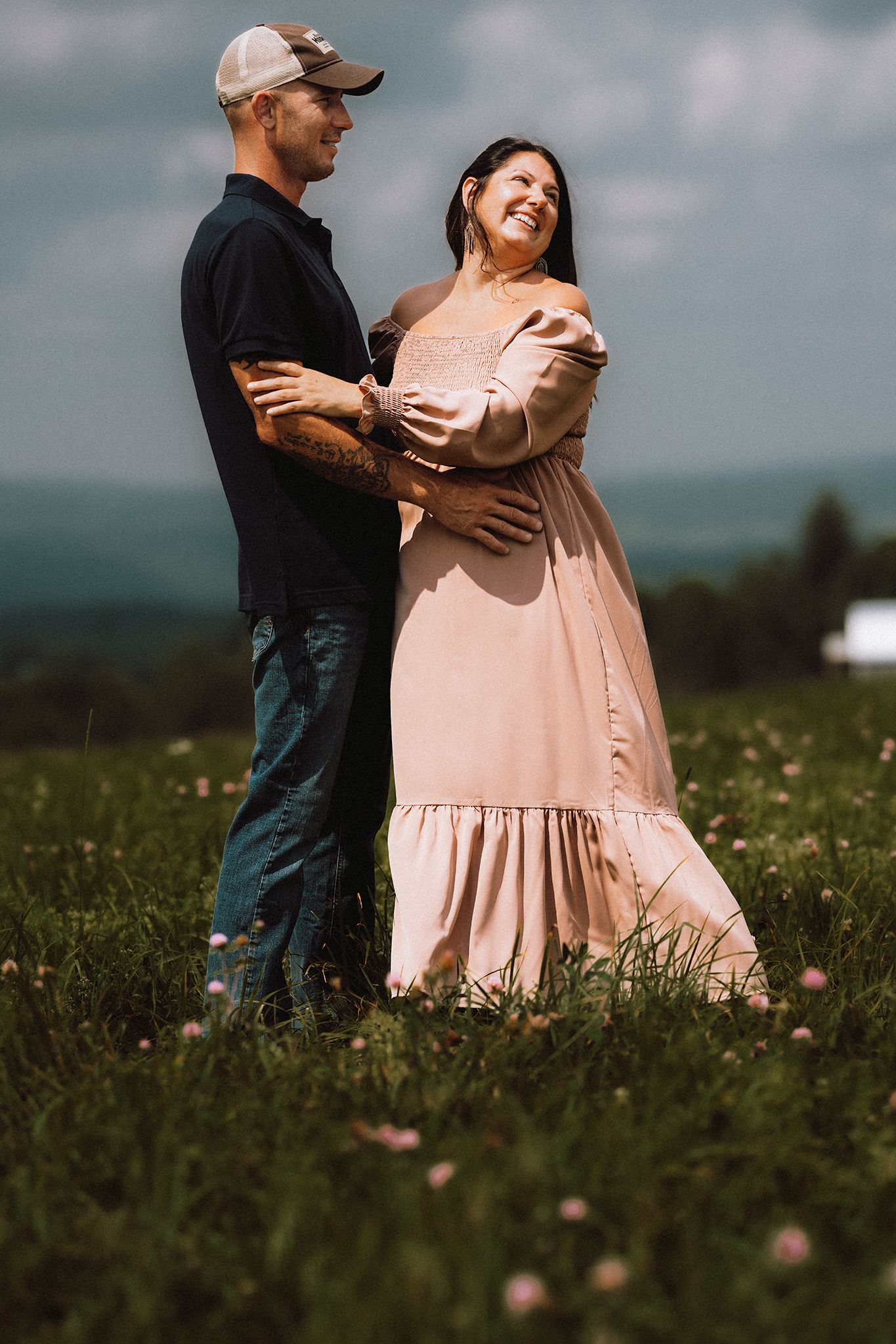 Couple sharing intimate moment in field with woman wearing flowing pink dress.