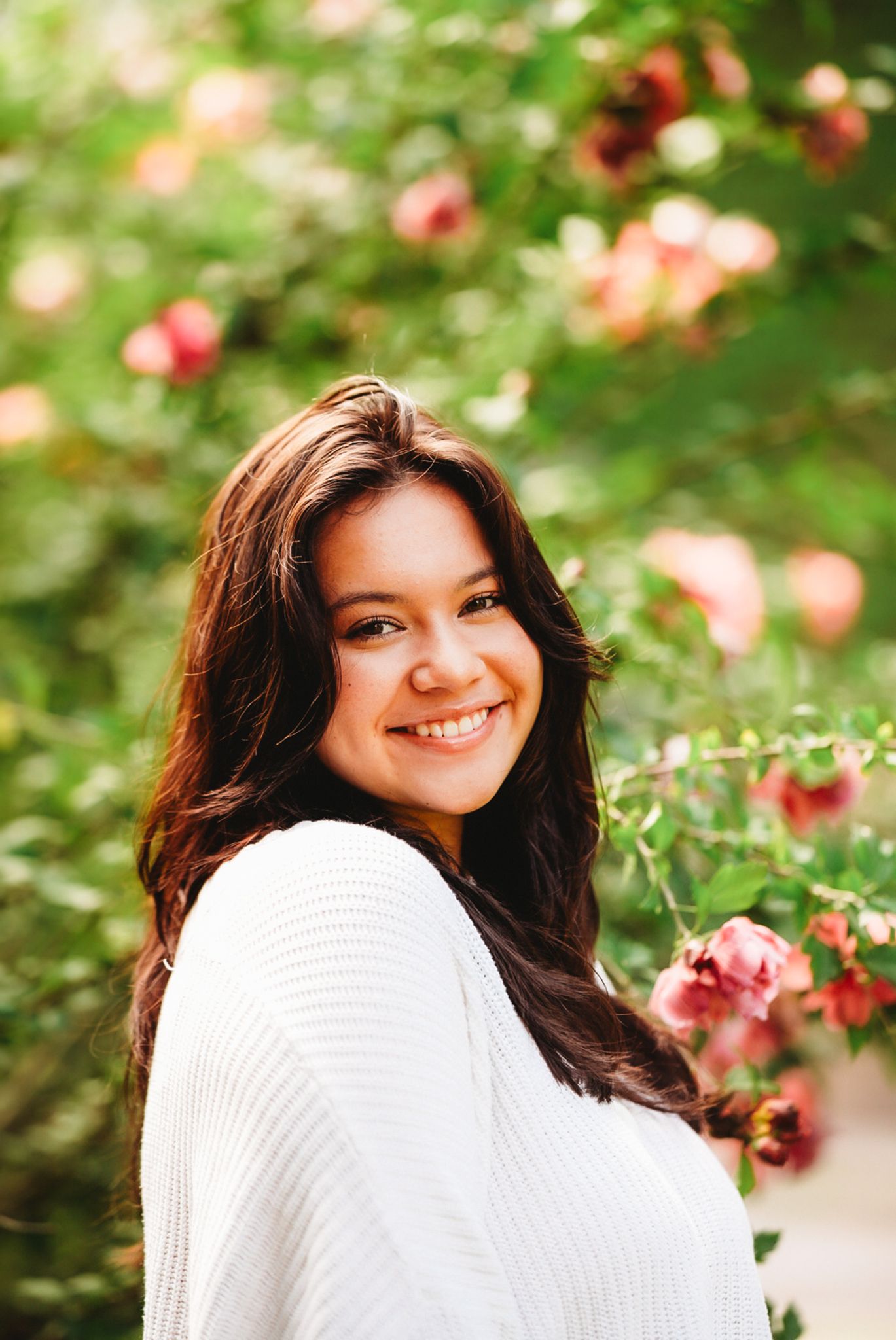 Portrait of woman smiling near blooming pink roses in garden.
