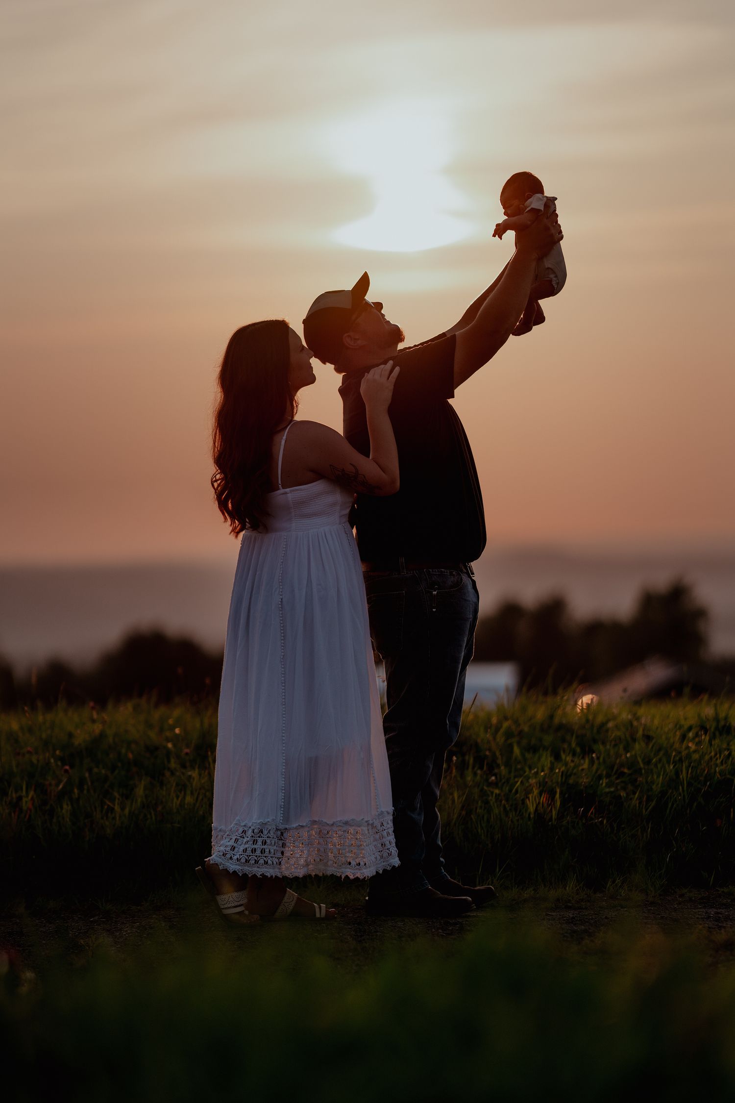 Silhouettes of a couple share an intimate moment at sunset in a field.