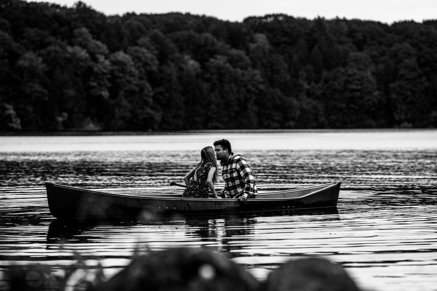 A silhouetted couple shares a romantic moment in a canoe on a peaceful lake.