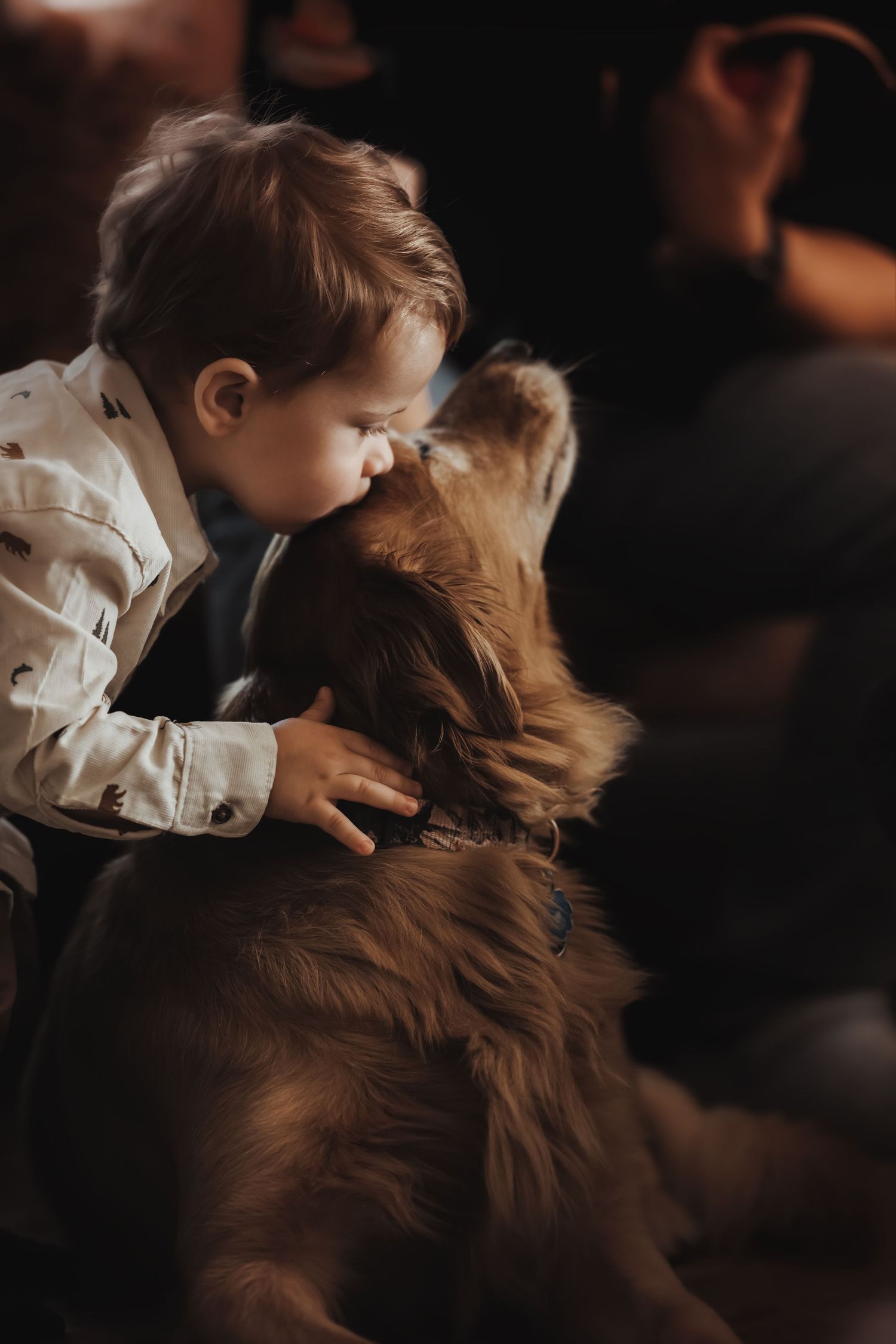A child in white gently embraces a fluffy brown dog in a candid moment.