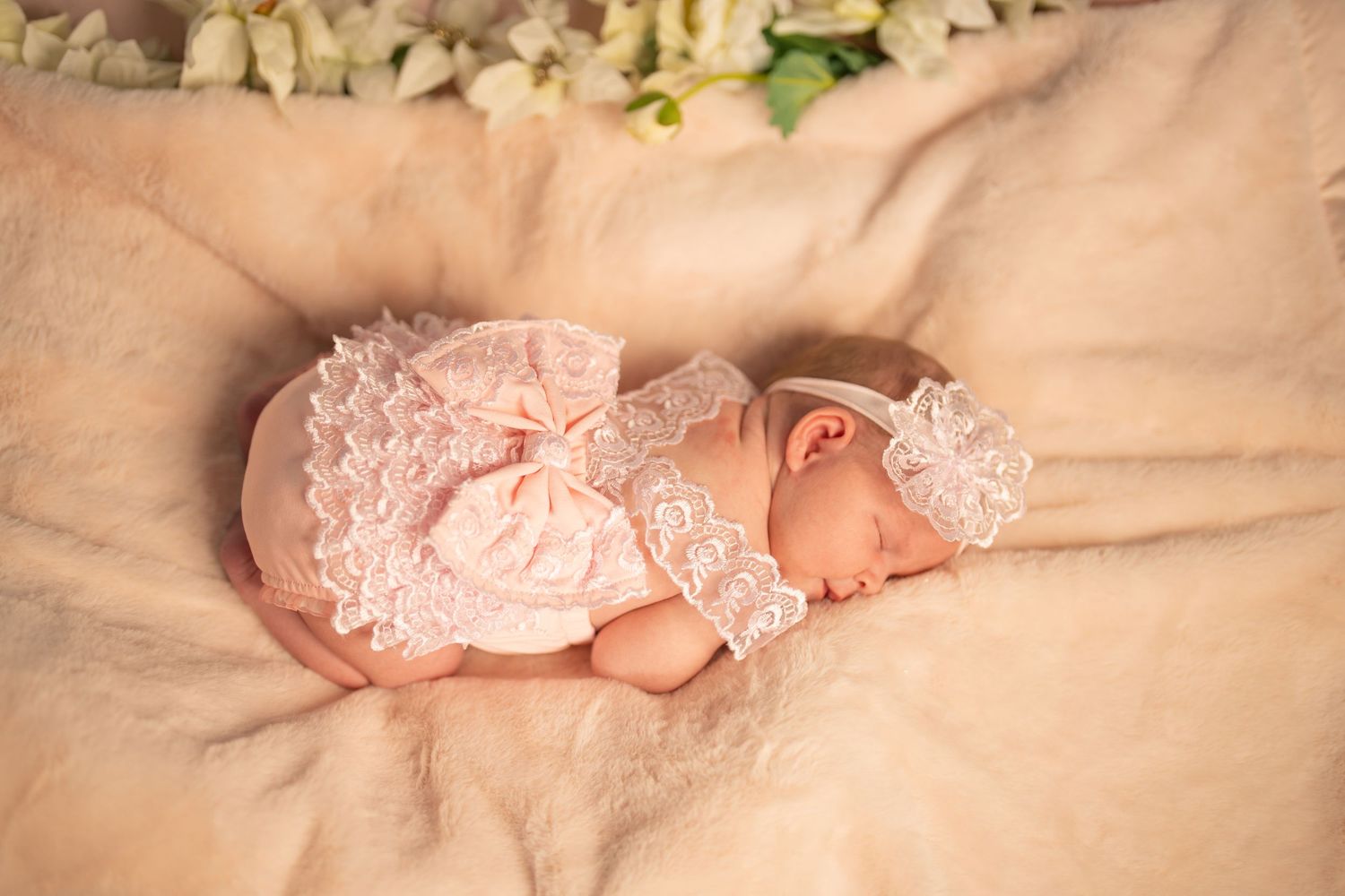 Delicate newborn photography featuring soft pink lace details against cream background.
