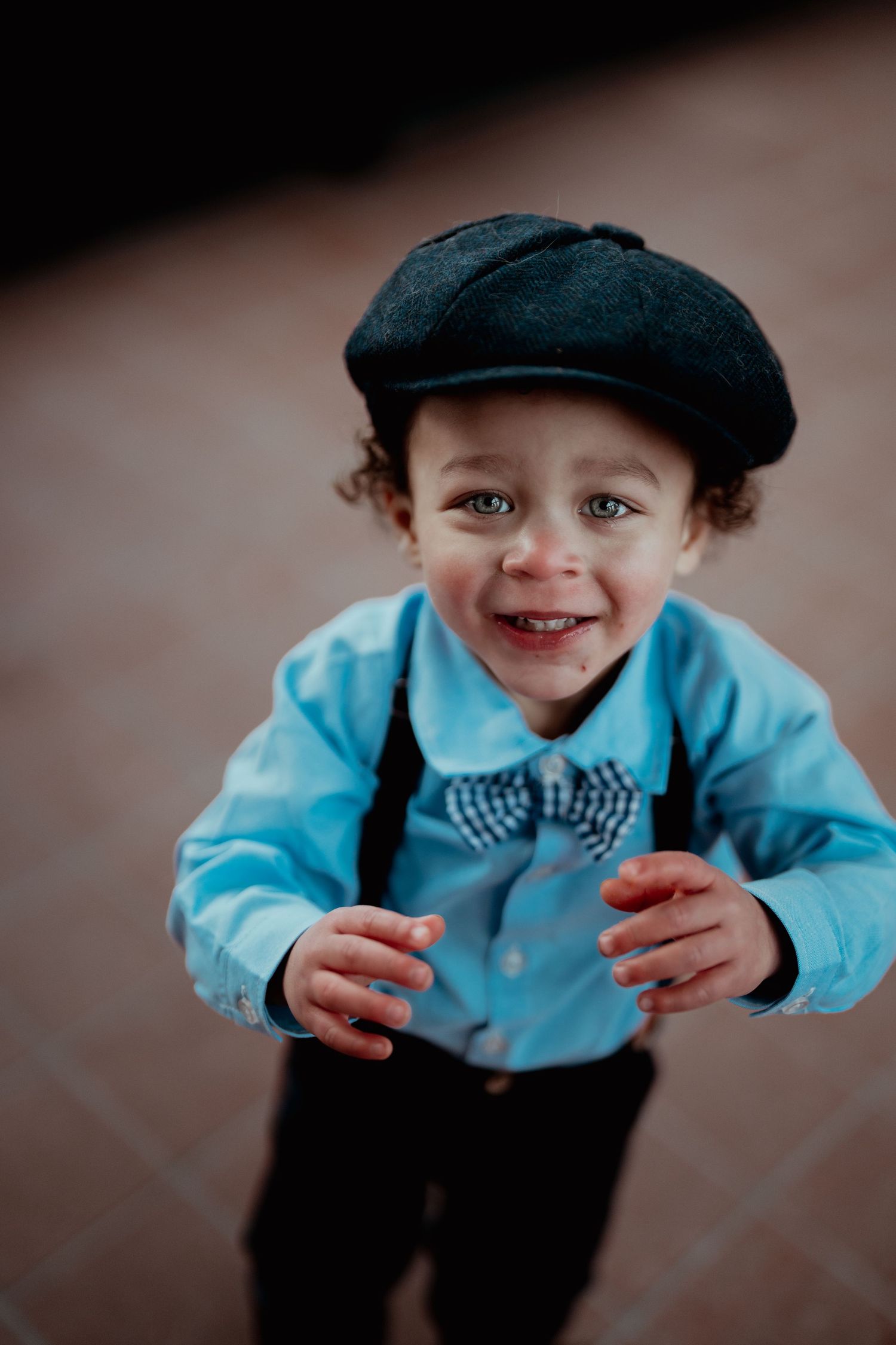 A small child in a blue jacket and newsboy cap smiles brightly at the camera.