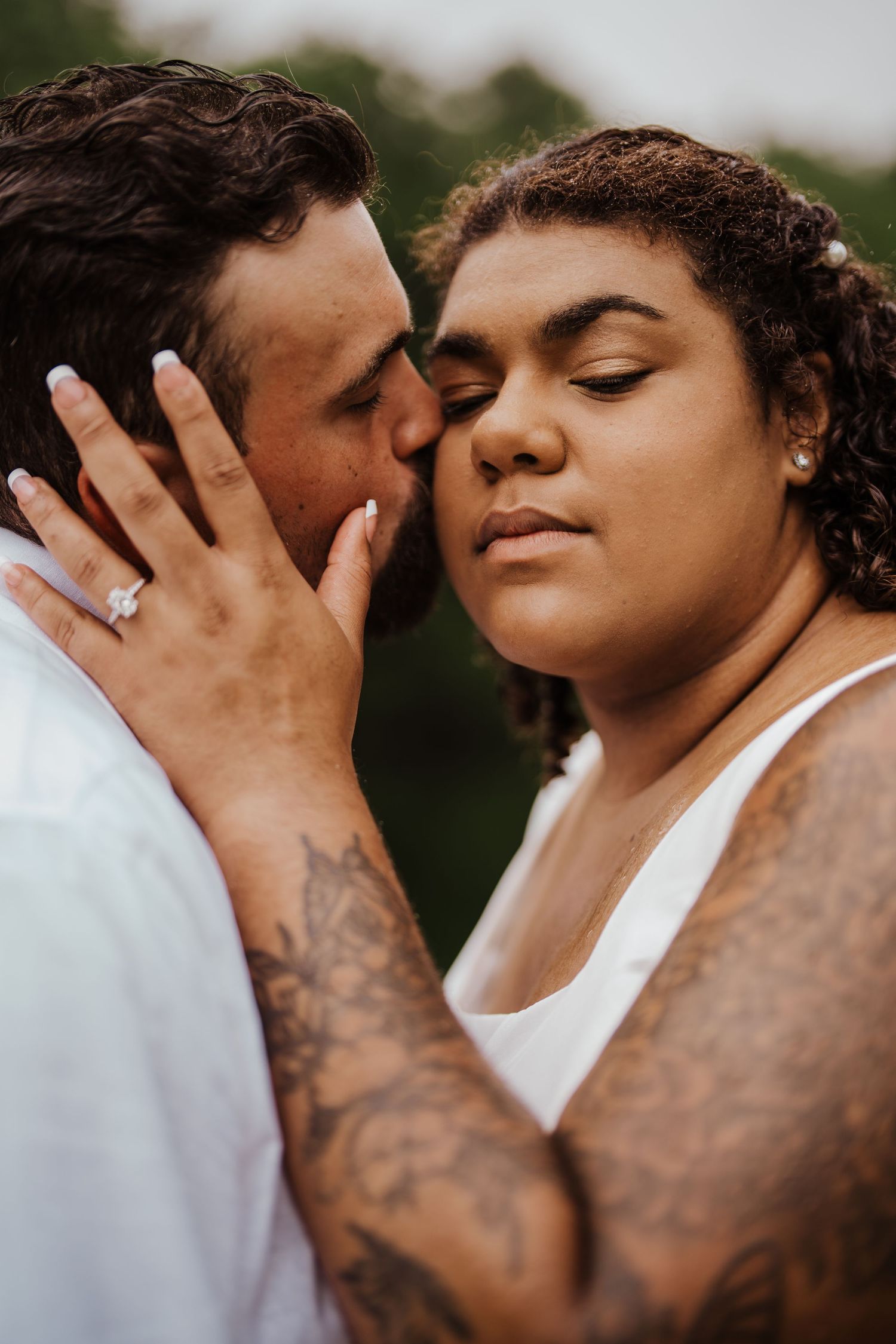 Intimate romantic moment captured between couple with visible tattoos and engagement ring.