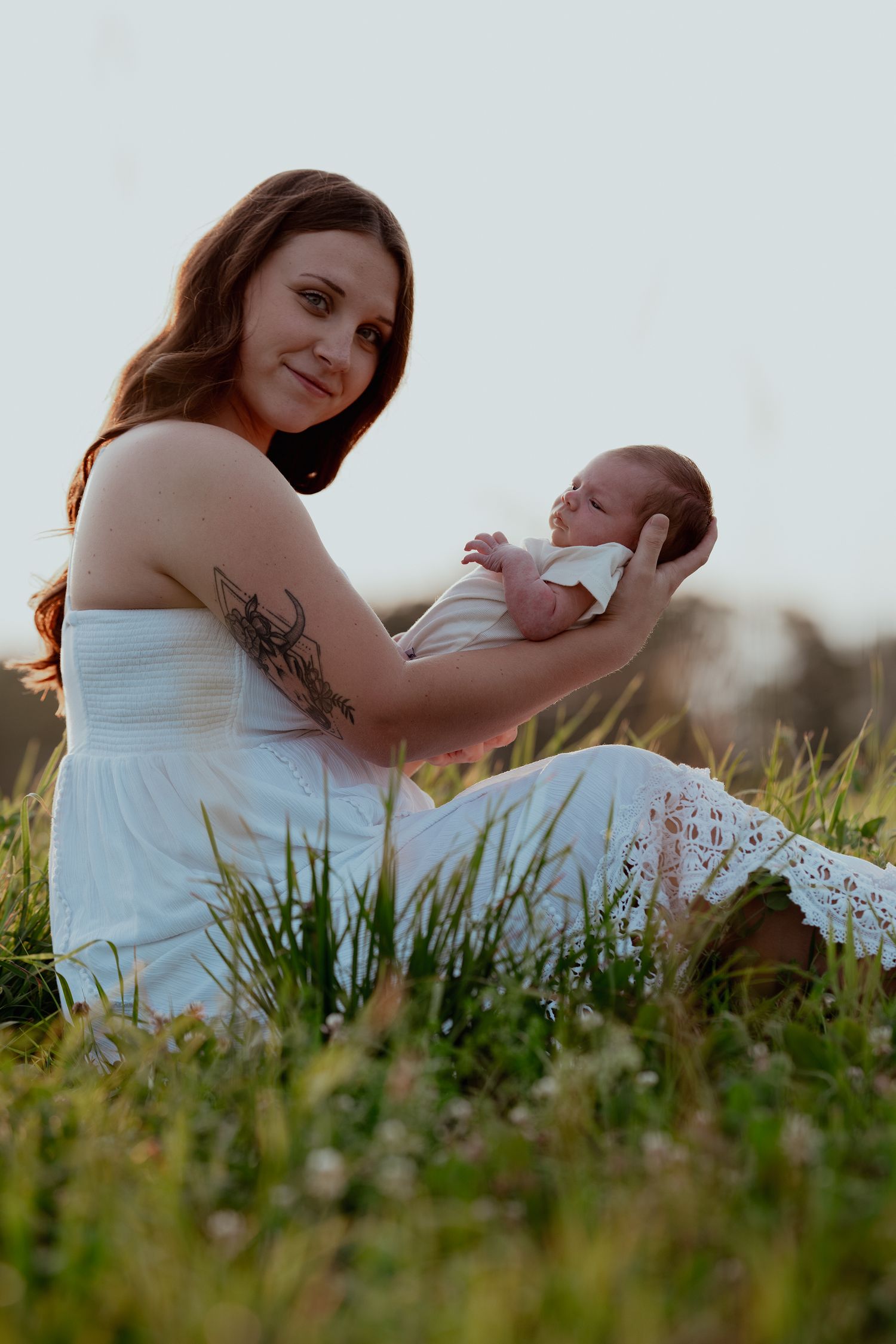 A tender moment between parent and baby while sitting in a grassy field at sunset.