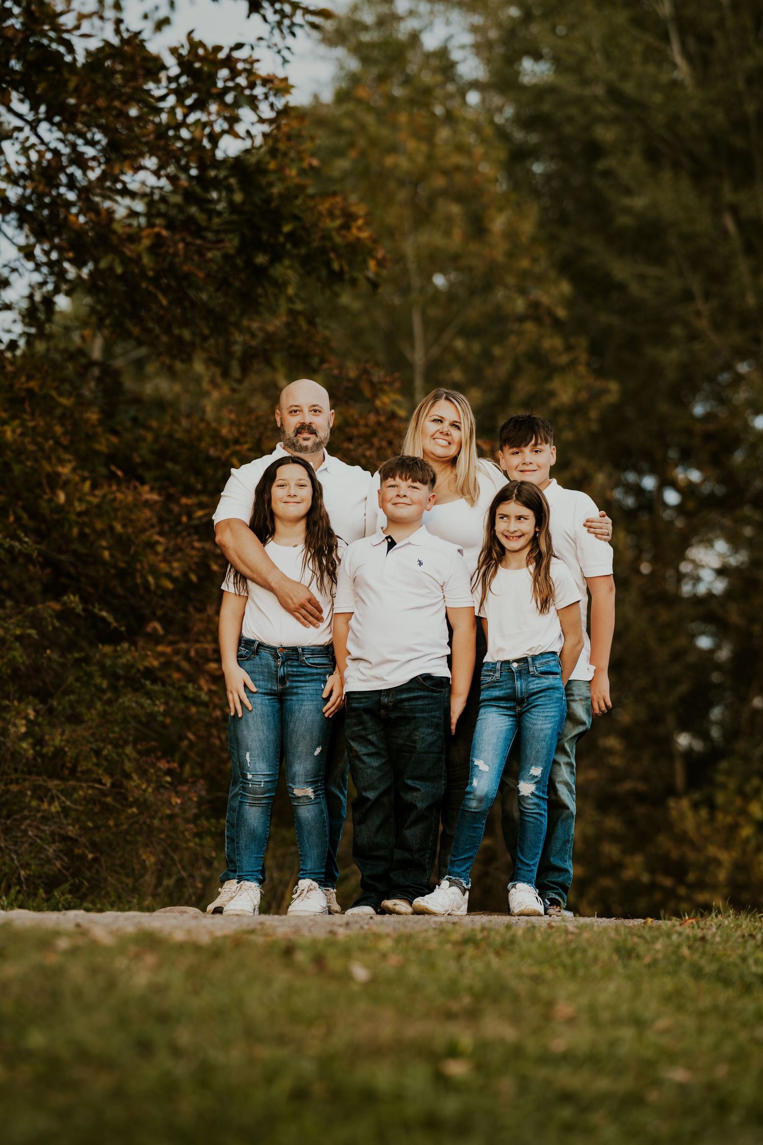 Four friends sit together wearing coordinated denim and white outfits during an autumn outdoor photoshoot.