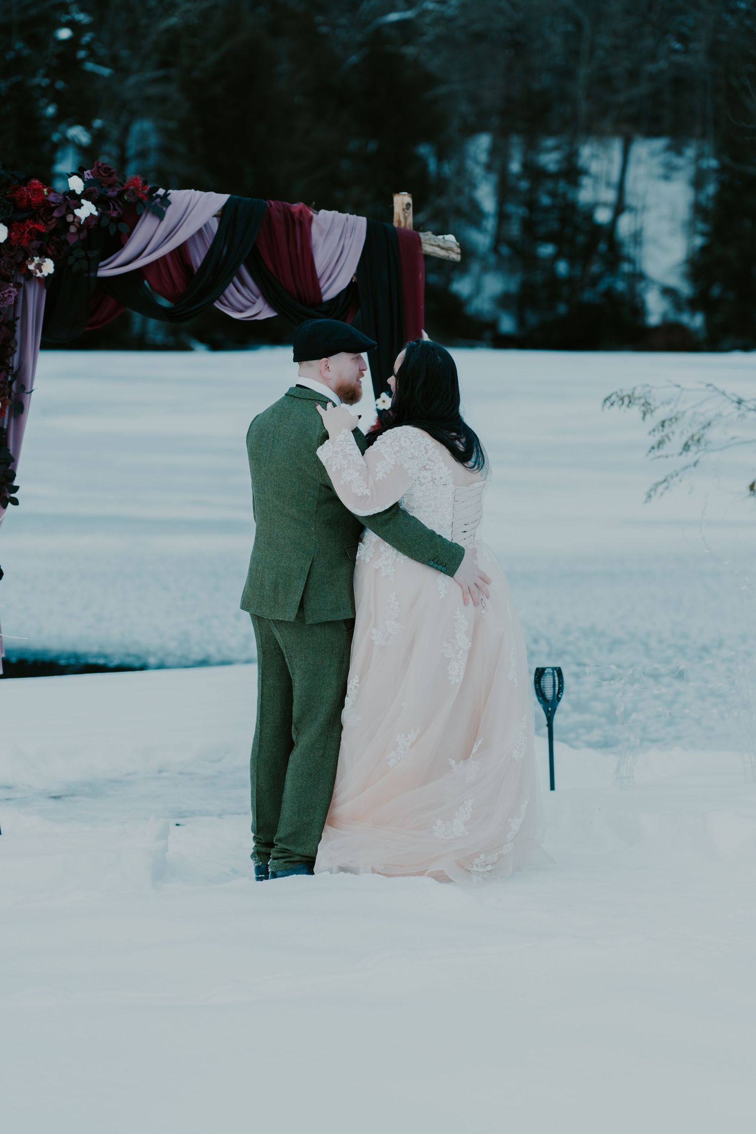 Romantic winter wedding scene with couple in snow against evergreen forest.