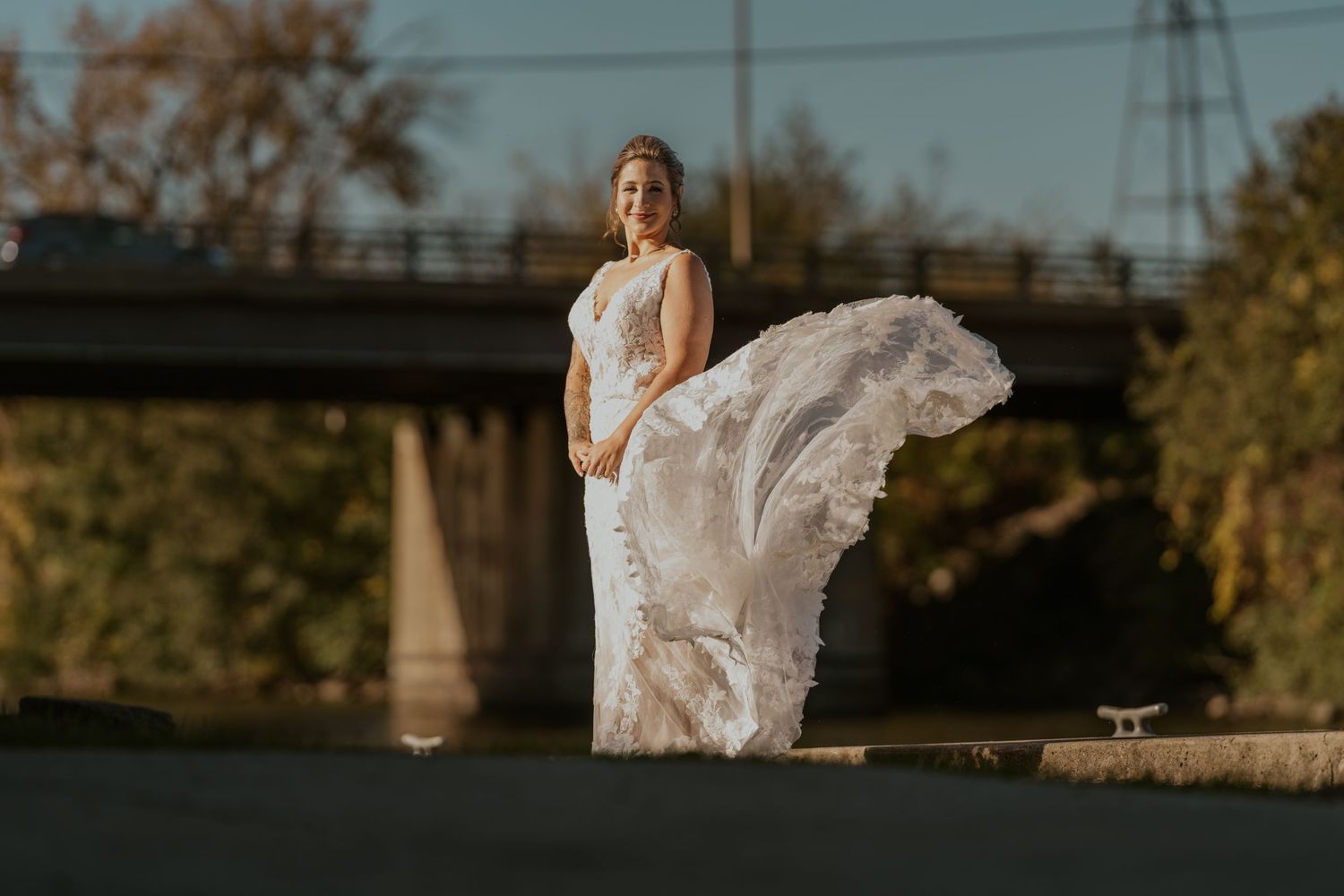 A bride in a lace gown poses during golden hour outdoor wedding photography.