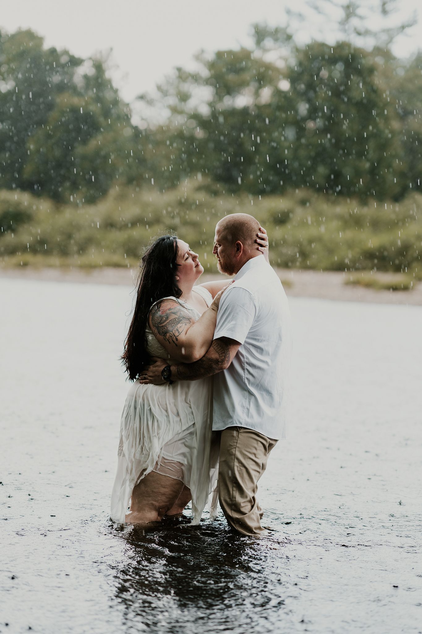 Romantic couple embracing while standing in shallow water during light rainfall.