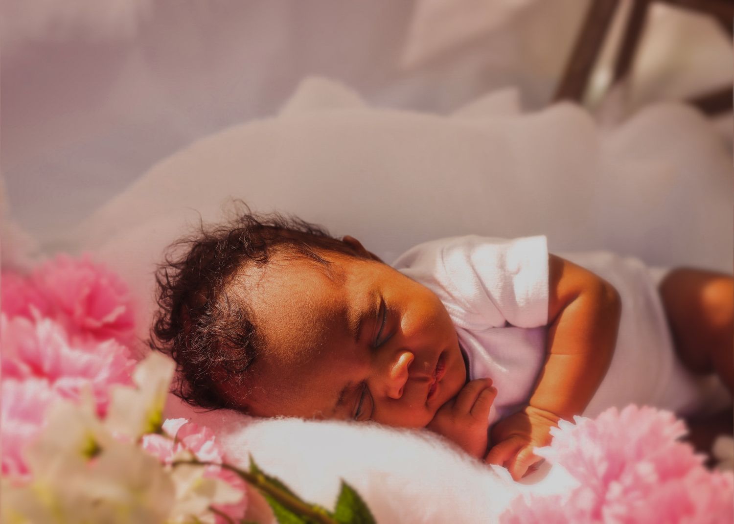 A close-up portrait of a sleeping baby surrounded by delicate pink flowers.