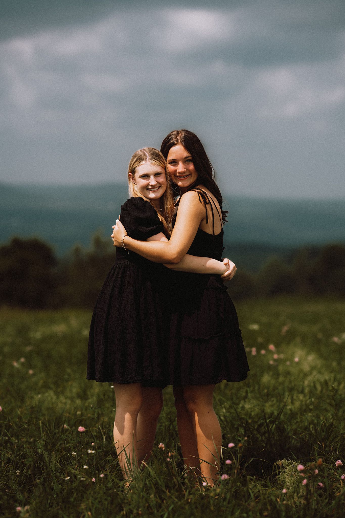 Friends share hugs and laughter in a sunlit meadow with wildflowers.