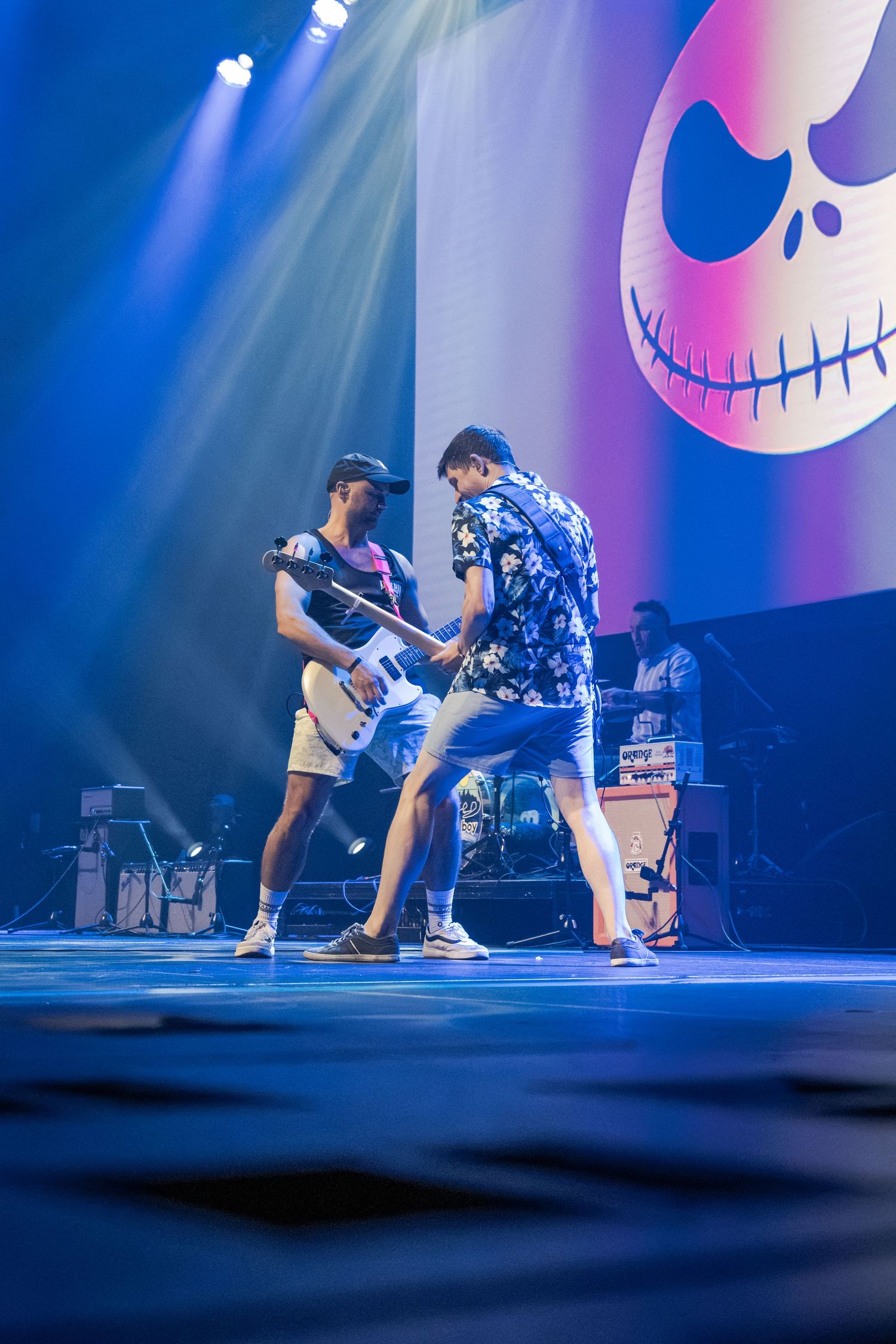 Two musicians perform on a blue-lit stage with a Nightmare Before Christmas skull backdrop.