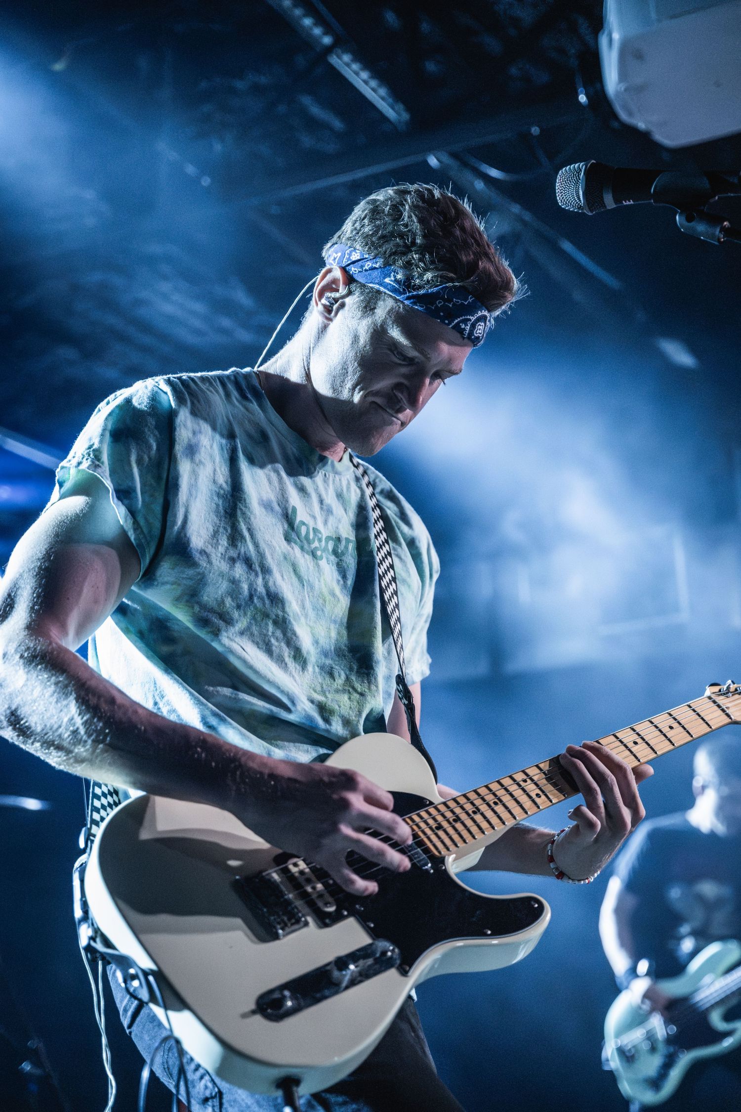 Guitarist playing a white electric guitar under moody blue stage lighting.
