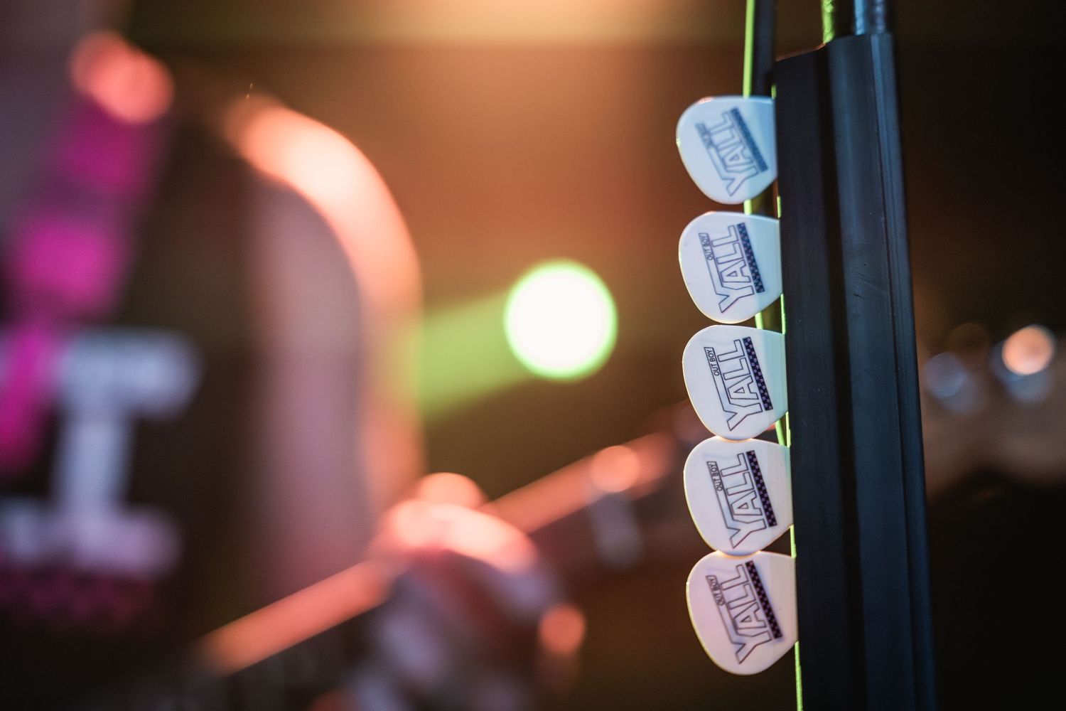 Guitar picks lined up on a microphone stand with blurred stage lights in background.