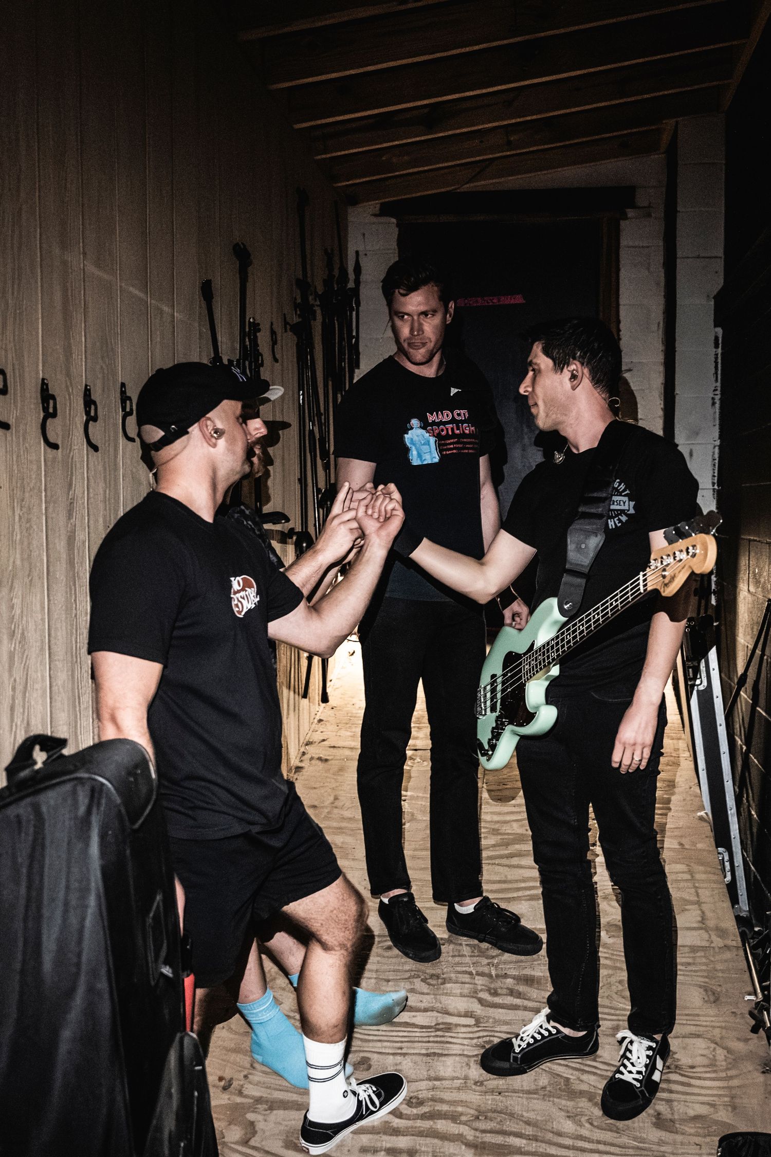 Band members wearing black gather backstage, sharing a moment with guitars and equipment visible in the background.