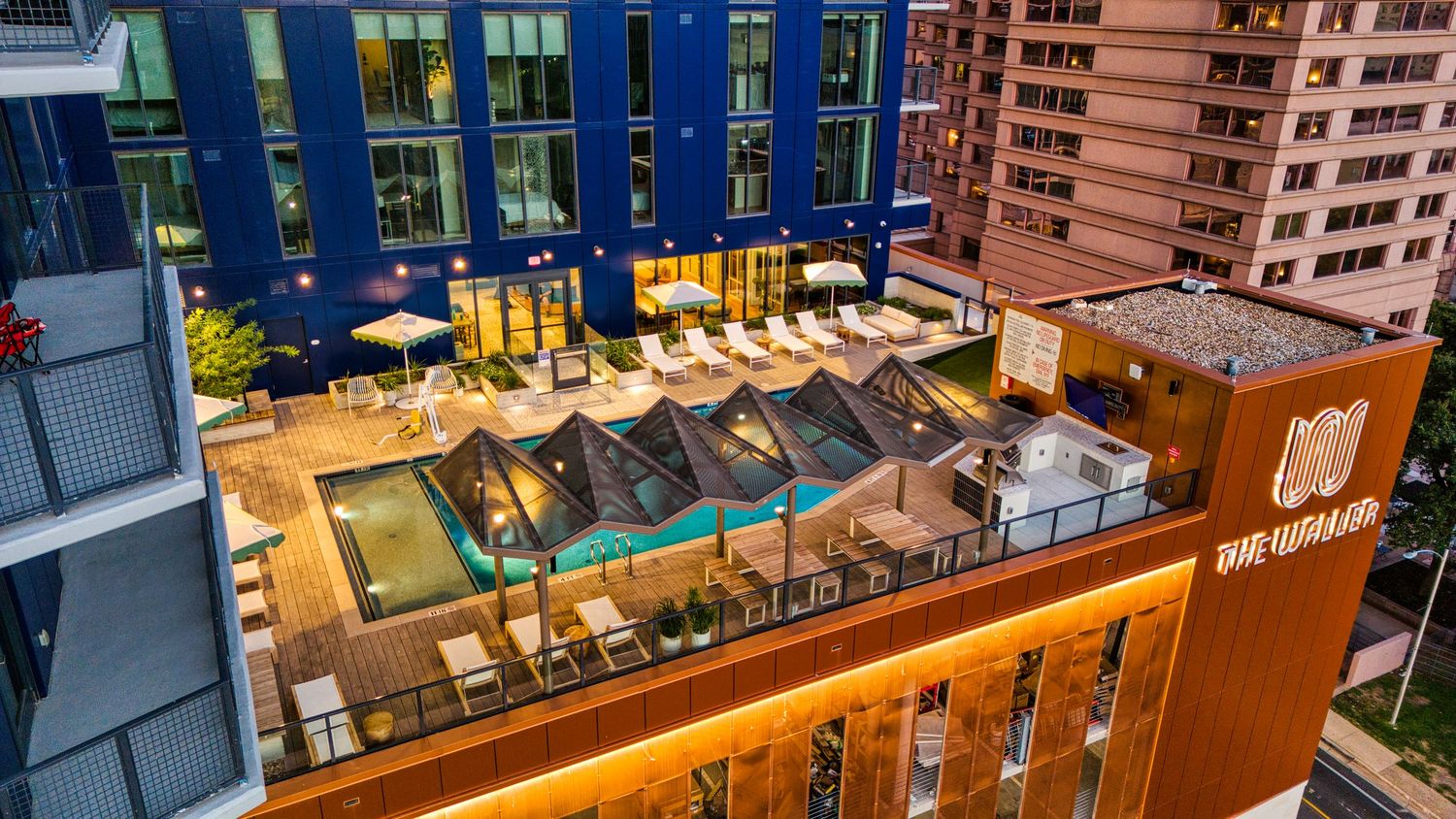 Daytime aerial view of urban rooftop pool deck with lounge chairs and modern amenities.