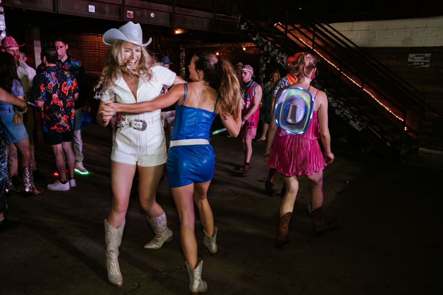 Festive partygoers dance together at a dimly lit indoor venue with colorful outfits.