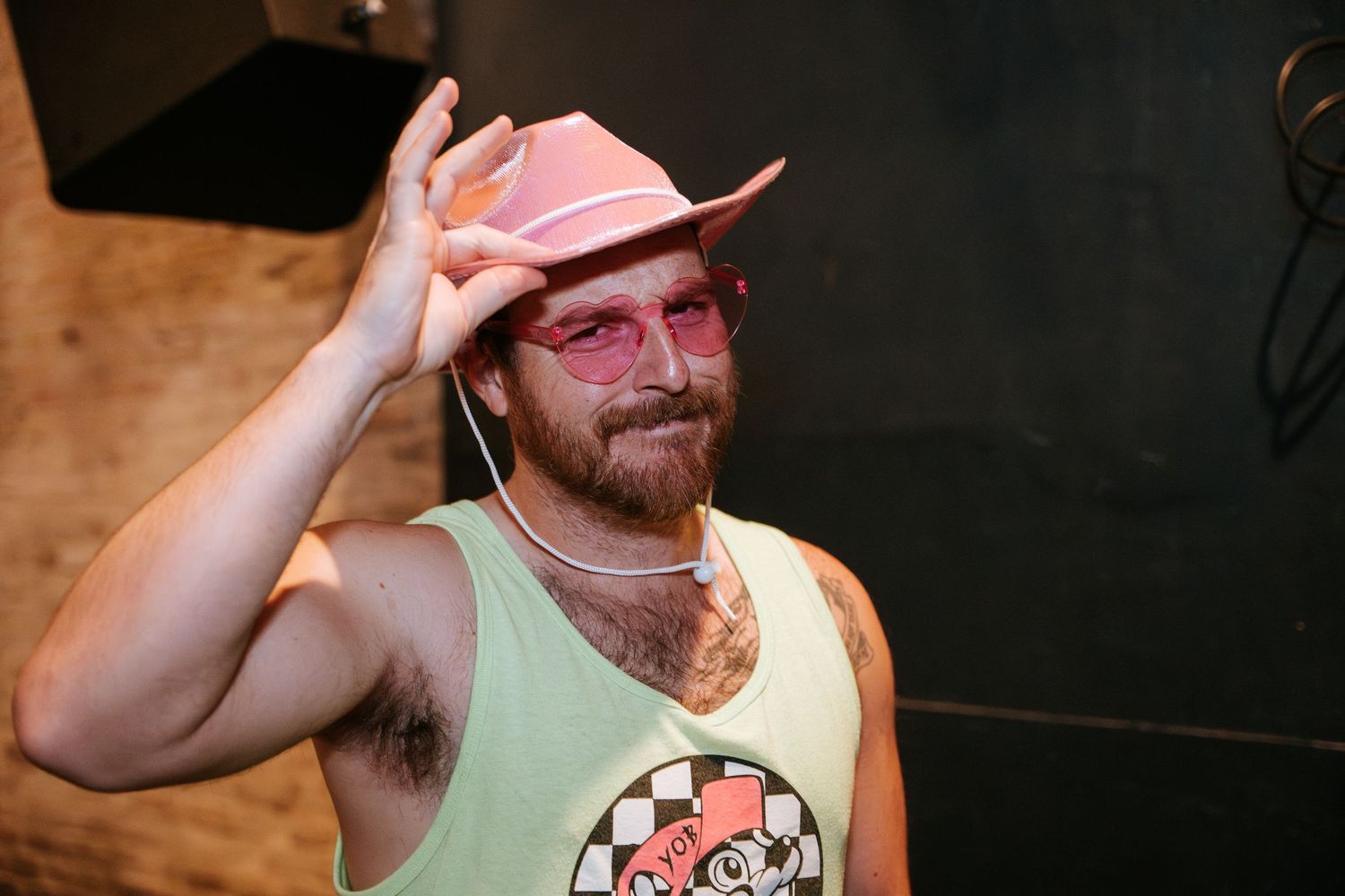 Partygoer in tank top and pink hat gestures while enjoying event.
