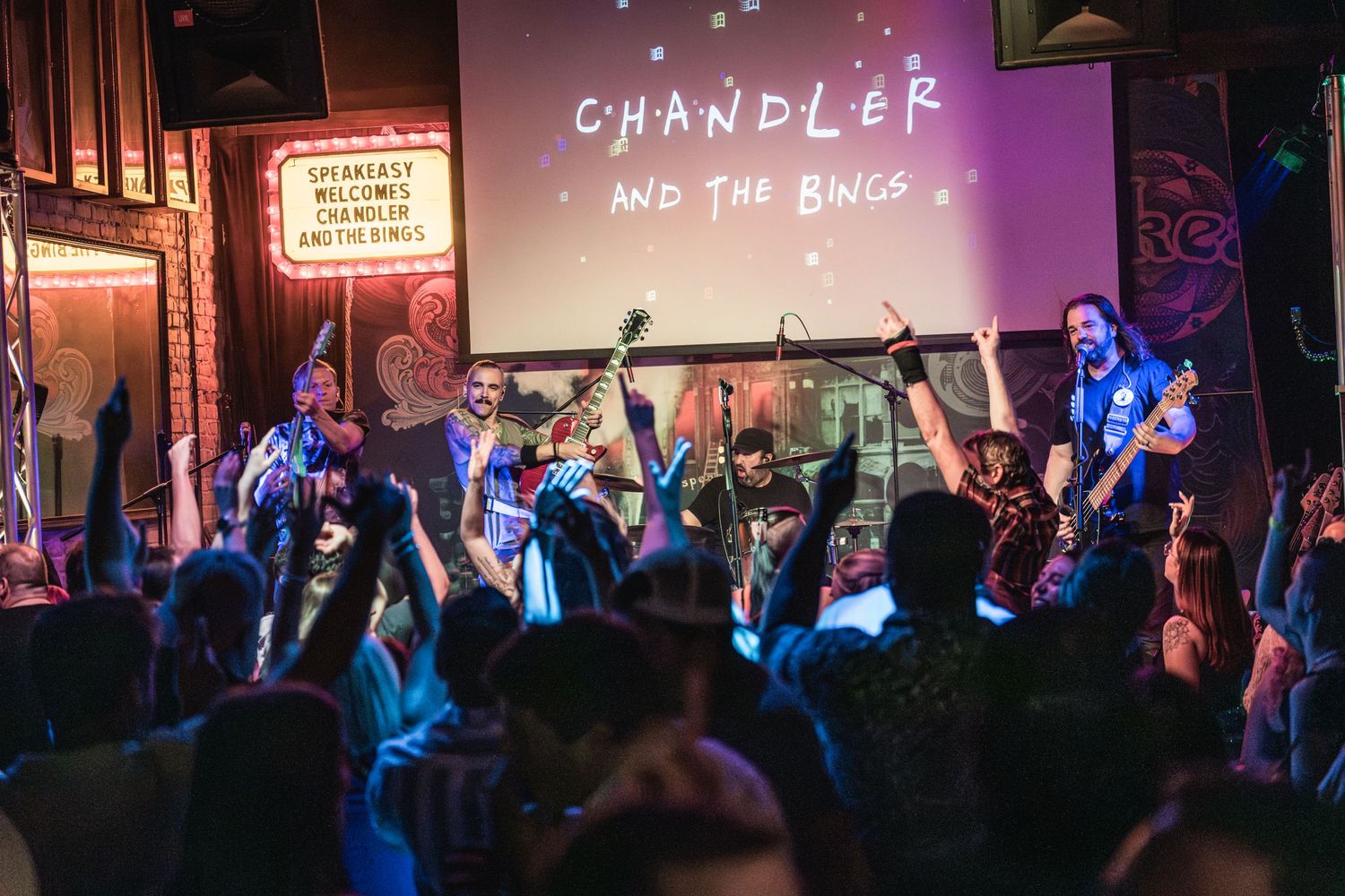 An energetic live music performance with a crowd under purple stage lights.