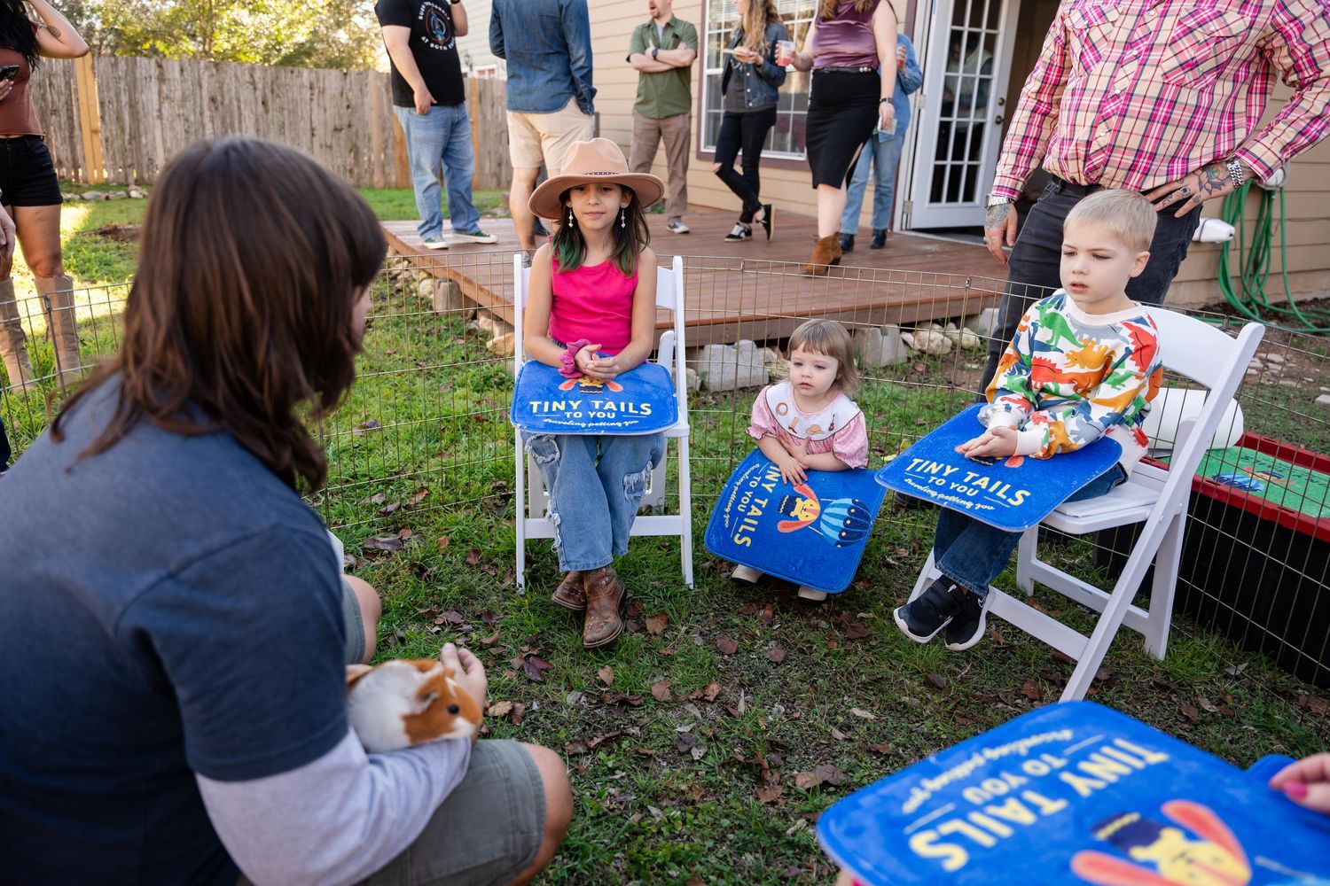 Children seated in lawn chairs at an outdoor gathering with blue bags in their laps.
