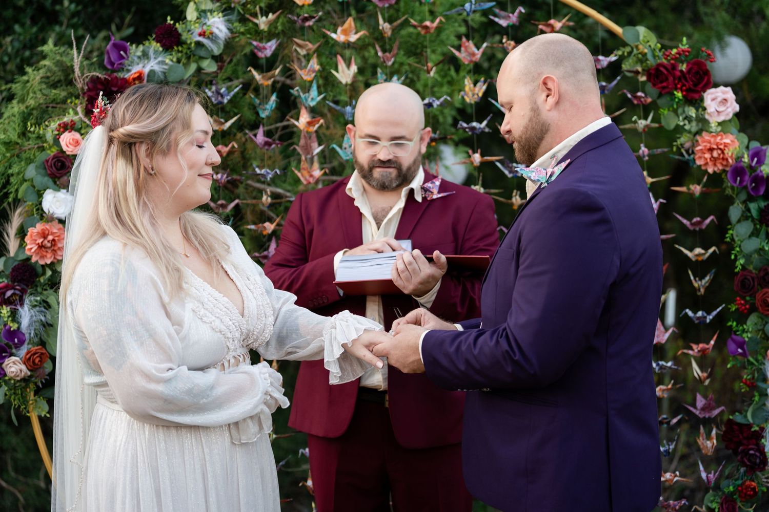 An outdoor wedding ceremony under an arch decorated with butterflies and floral arrangements.