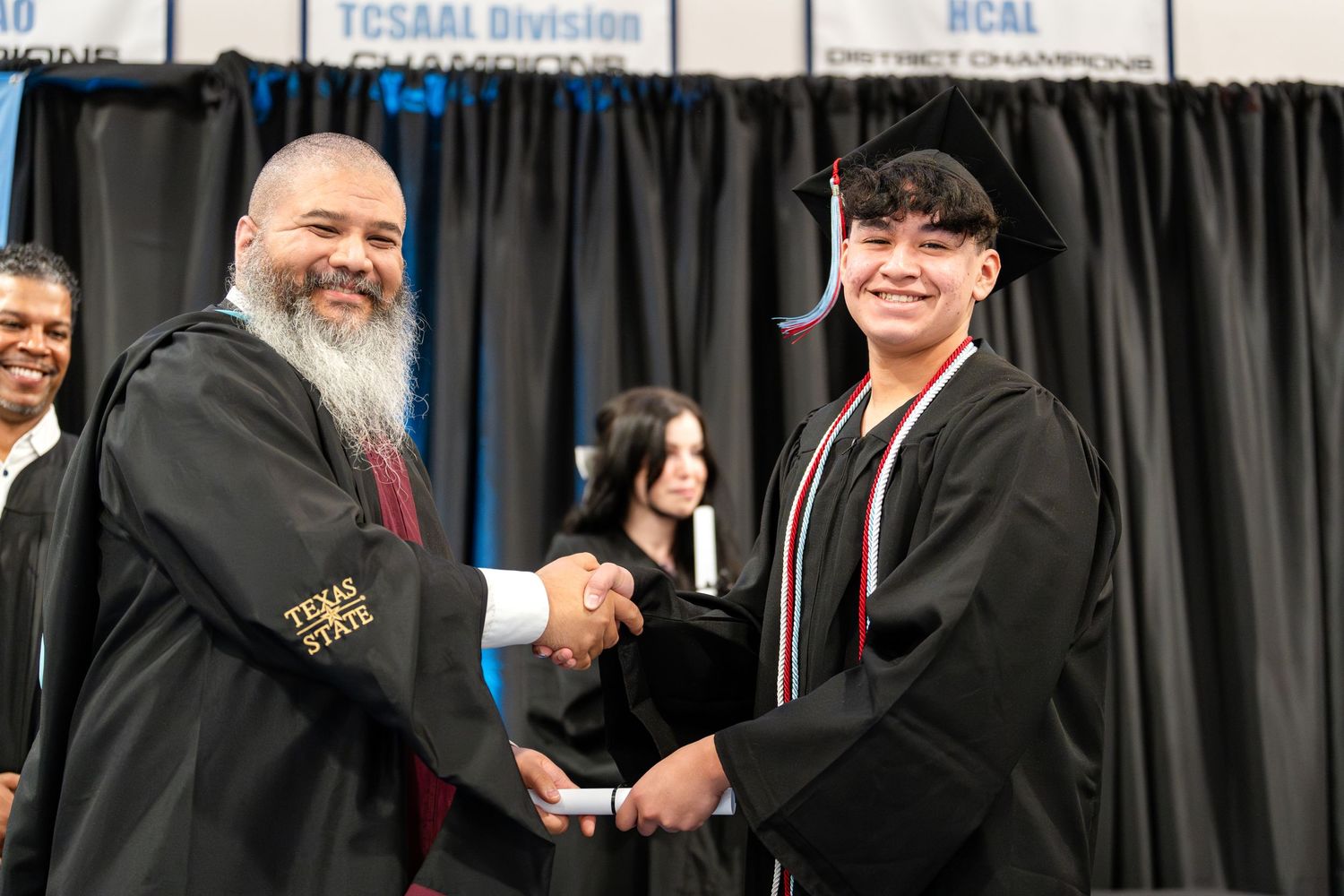 Graduate in black cap and gown shakes hands with faculty member during diploma presentation.