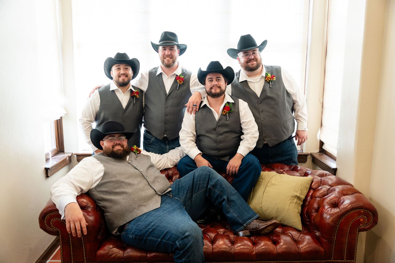 Group in western attire with grey vests and cowboy hats posed on leather couch.