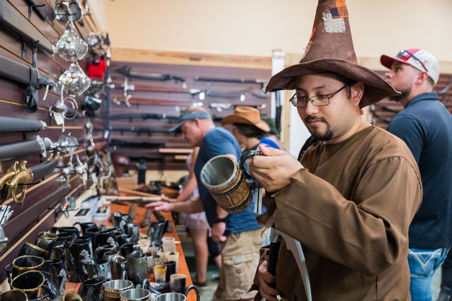 An attendee in a brown wizard hat examines merchandise at a Renaissance festival vendor booth.