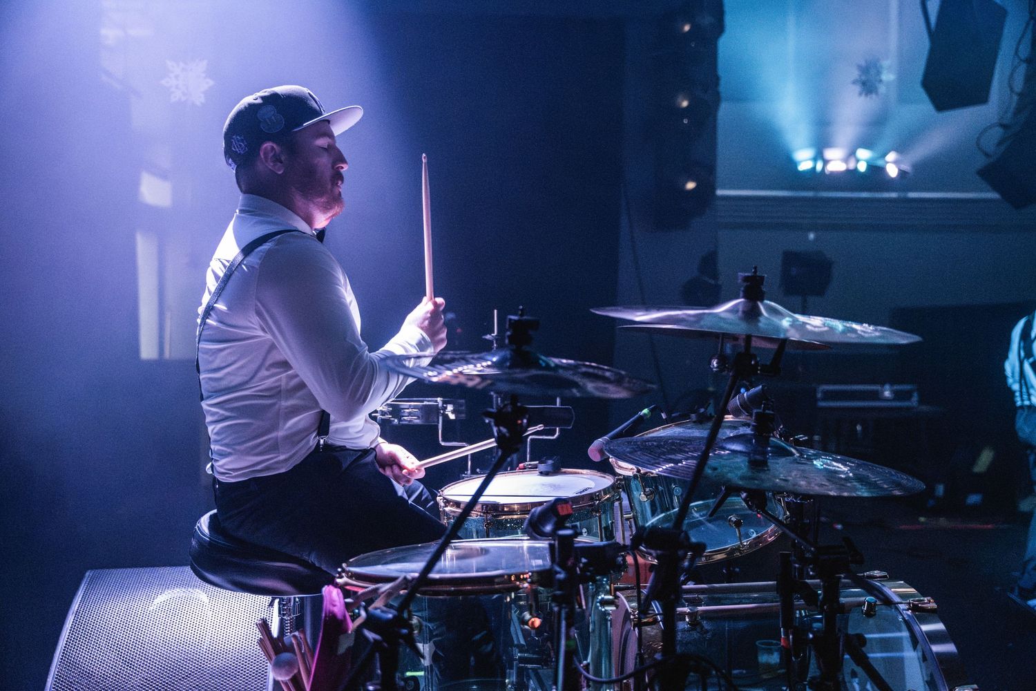 Drummer performs on stage surrounded by blue stage lighting.