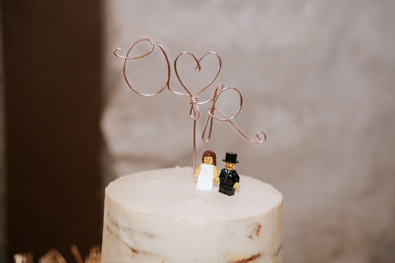 A minimalist white wedding cake topped with a delicate wire love heart decoration and small bride and groom figures.