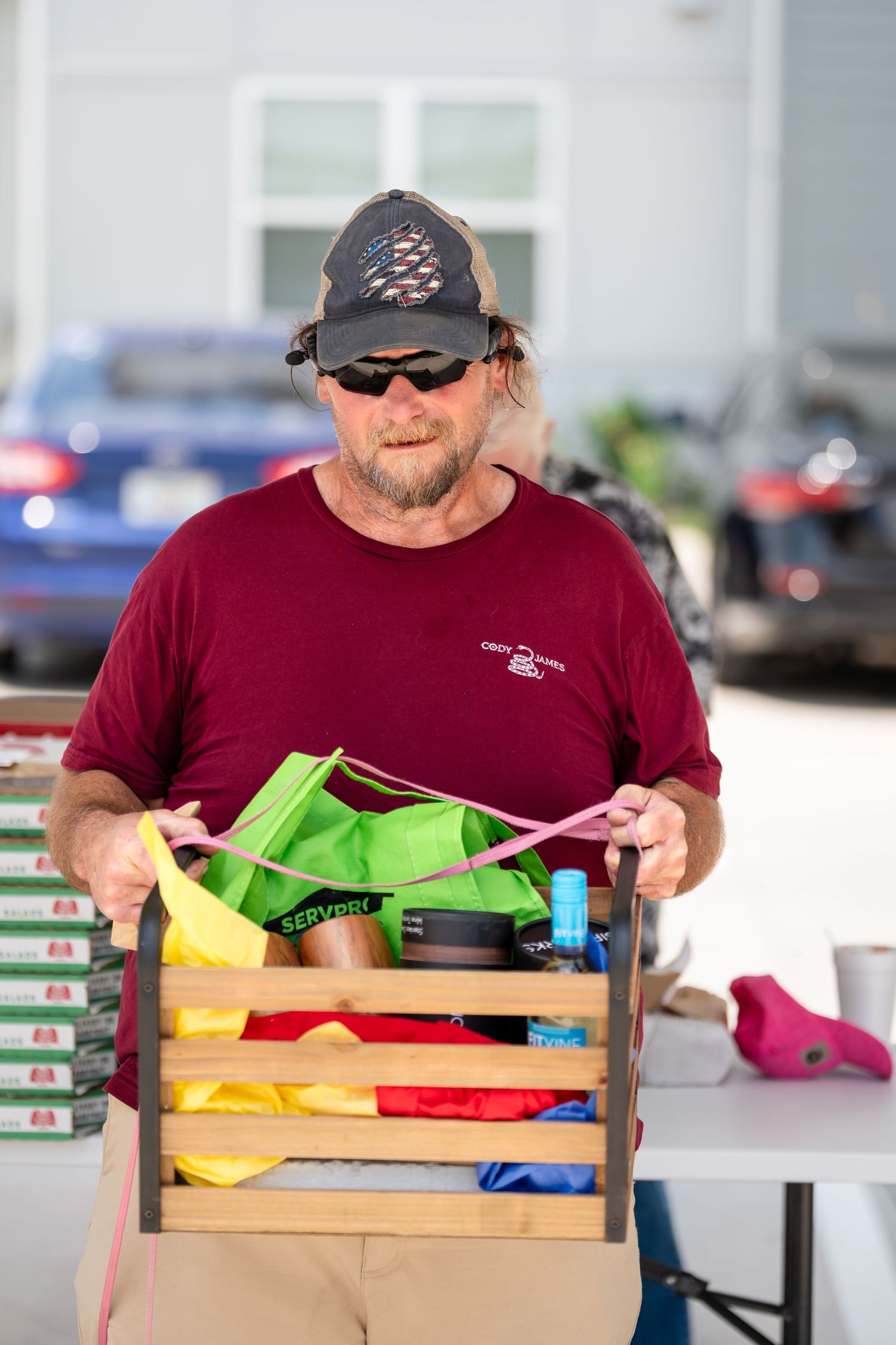 Person in red shirt and cap sorting through colorful pet supplies in wooden crates.