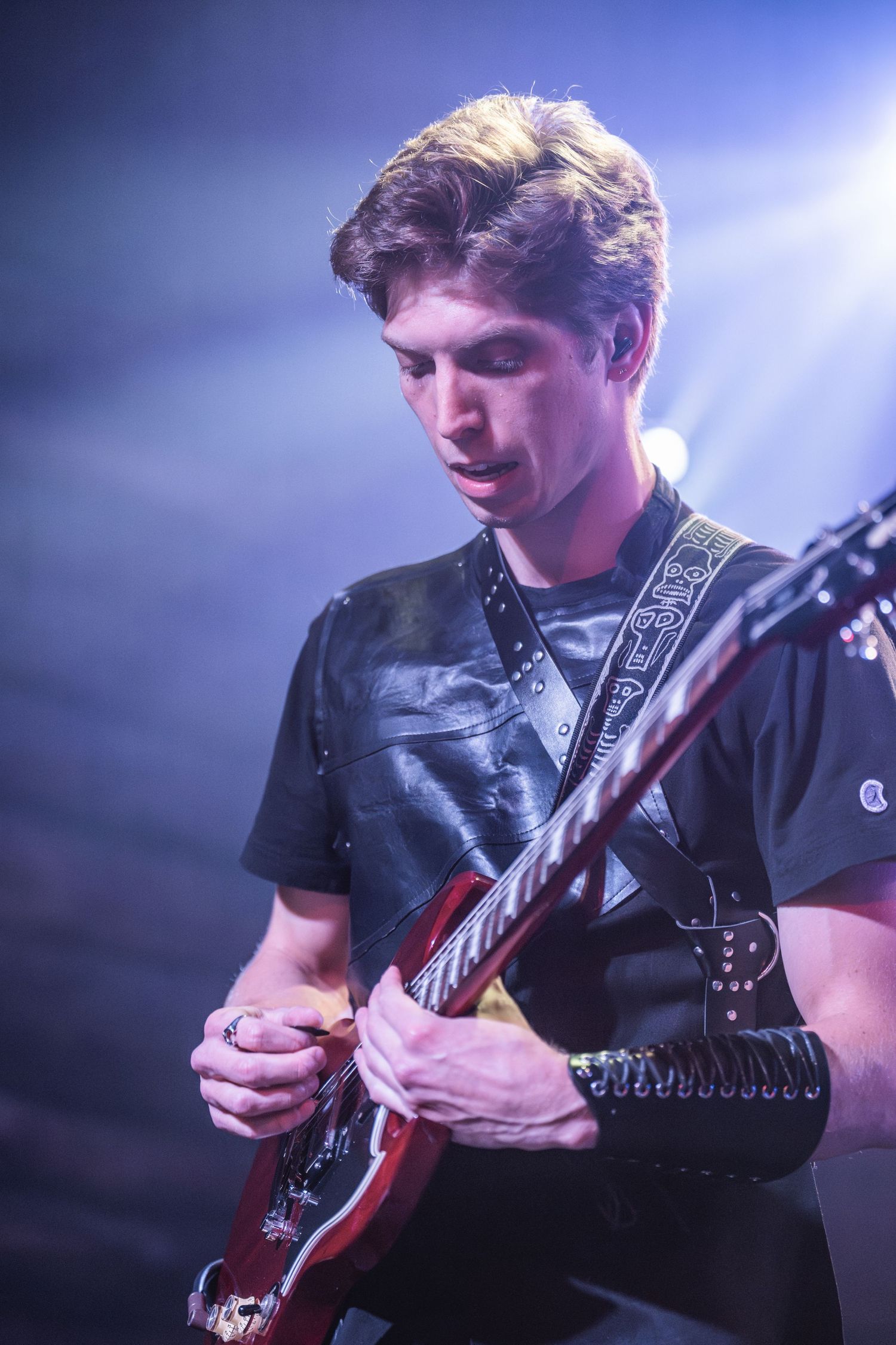 Guitarist performs intense solo on red electric guitar under blue stage lighting.