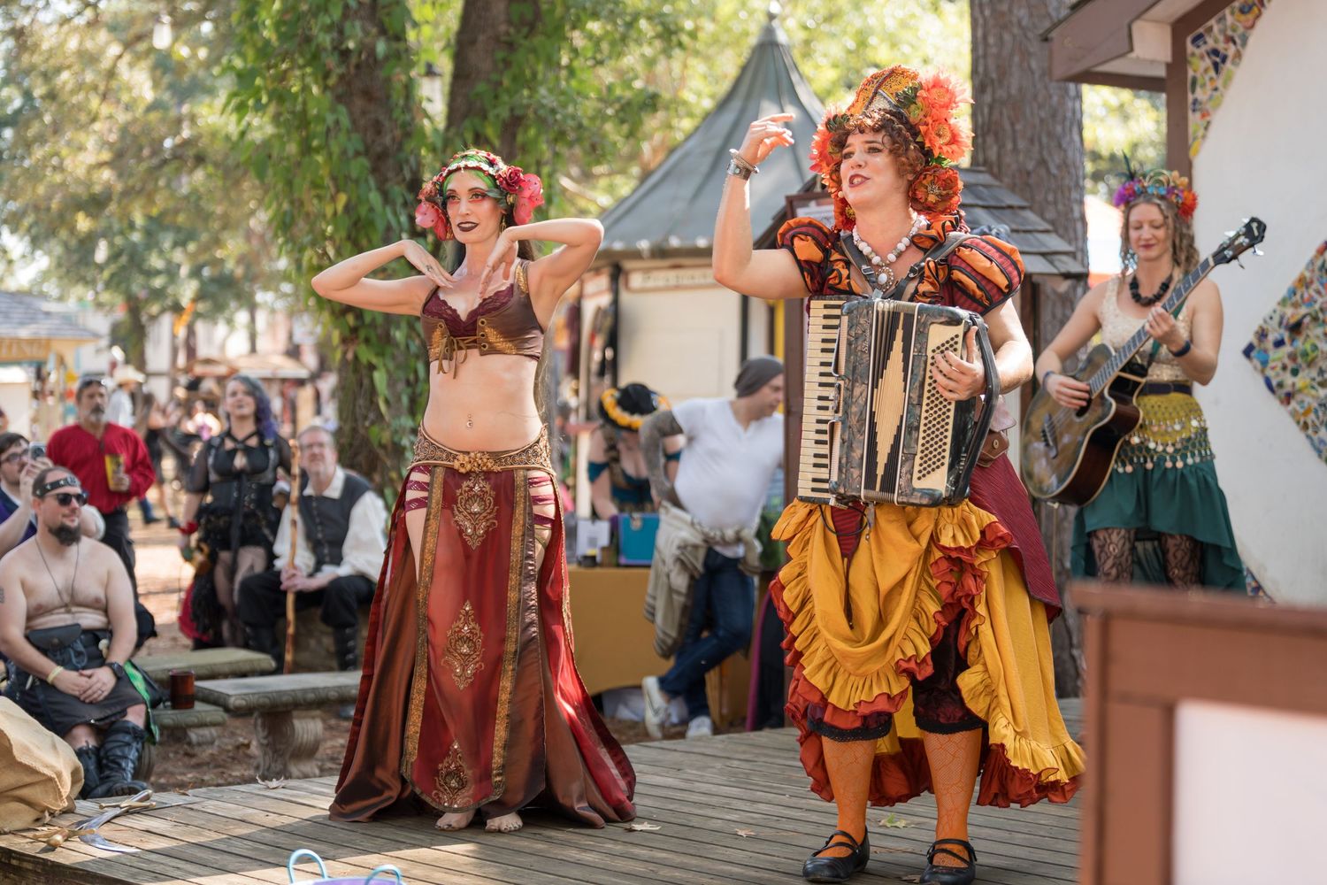 Performers in colorful renaissance costumes dance and play accordion at an outdoor festival.
