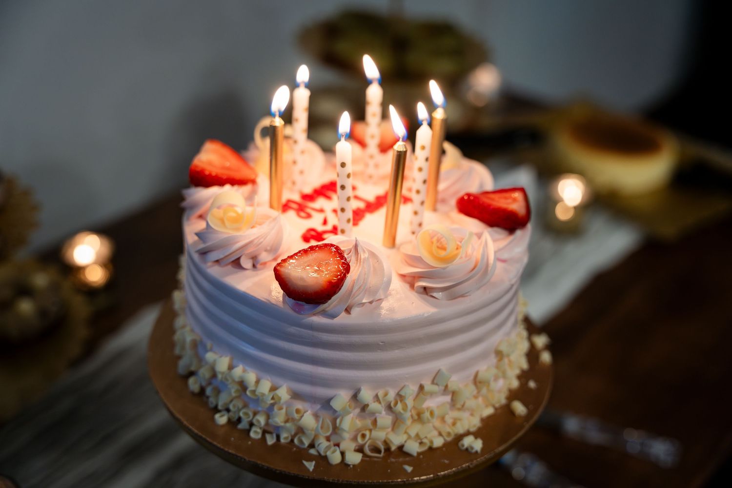 A festive birthday cake decorated with lit candles, purple frosting, and fresh strawberries on top.