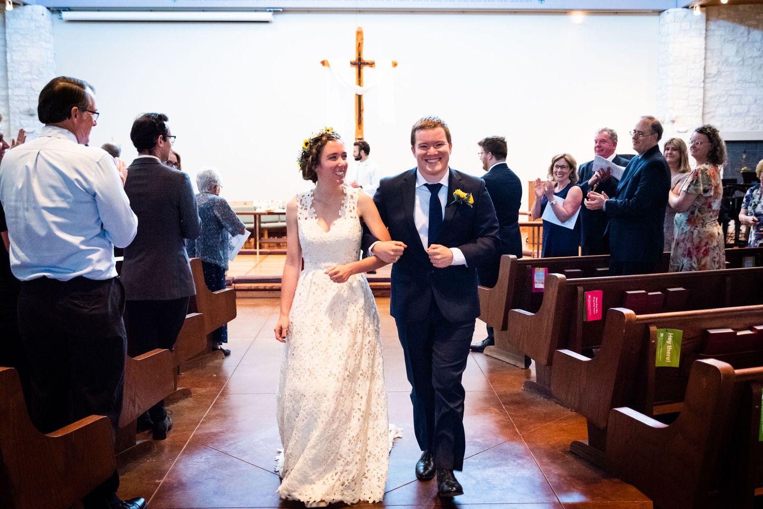 A couple walks down the church aisle after their wedding ceremony with guests looking on.