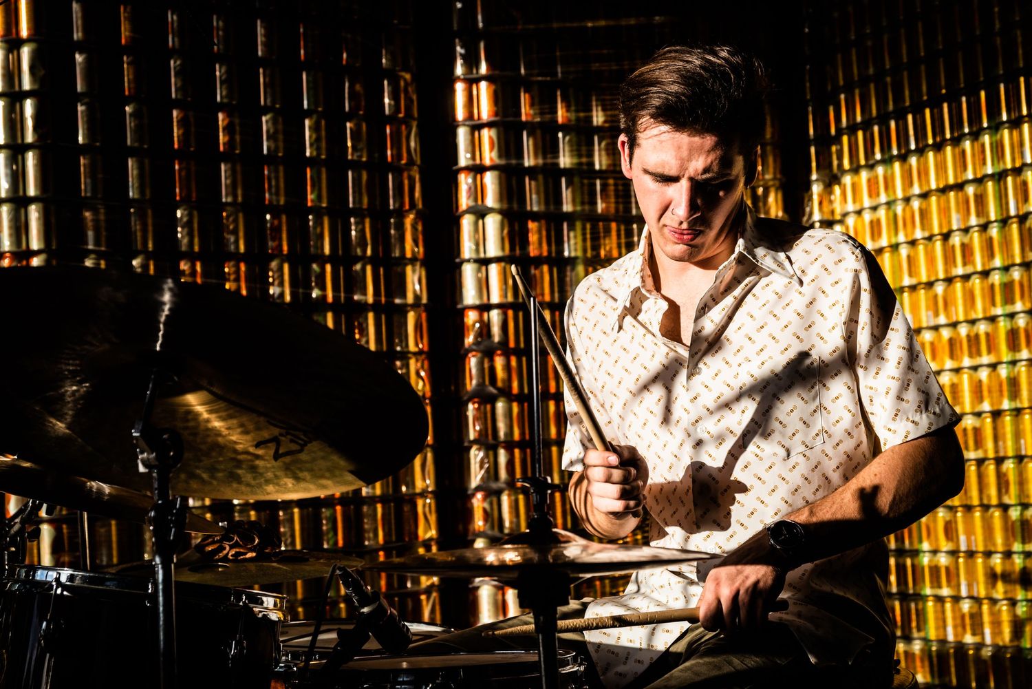 Drummer plays with intensity against gold-toned background during performance.