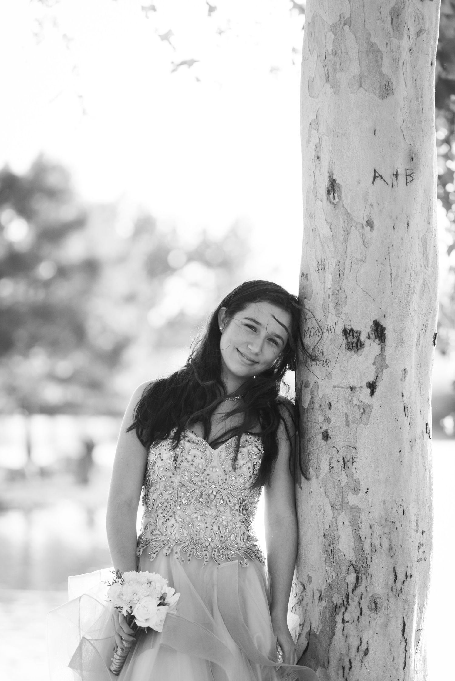 Black and white portrait of bride leaning against white tree trunk with bouquet.