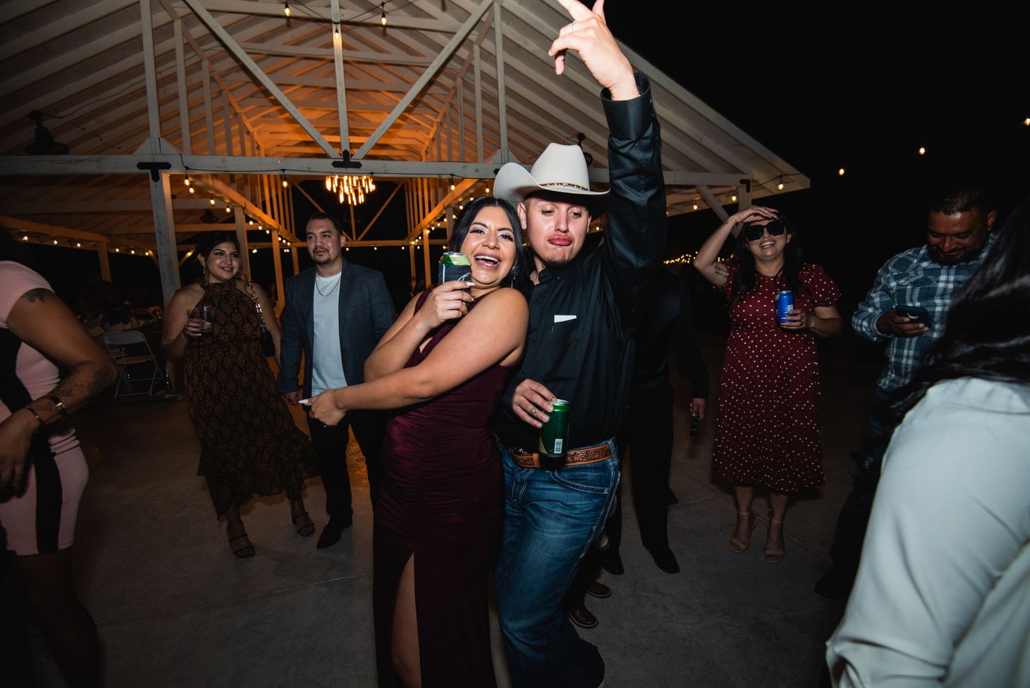 Wedding guests enjoy dancing together at a reception with string lights overhead.