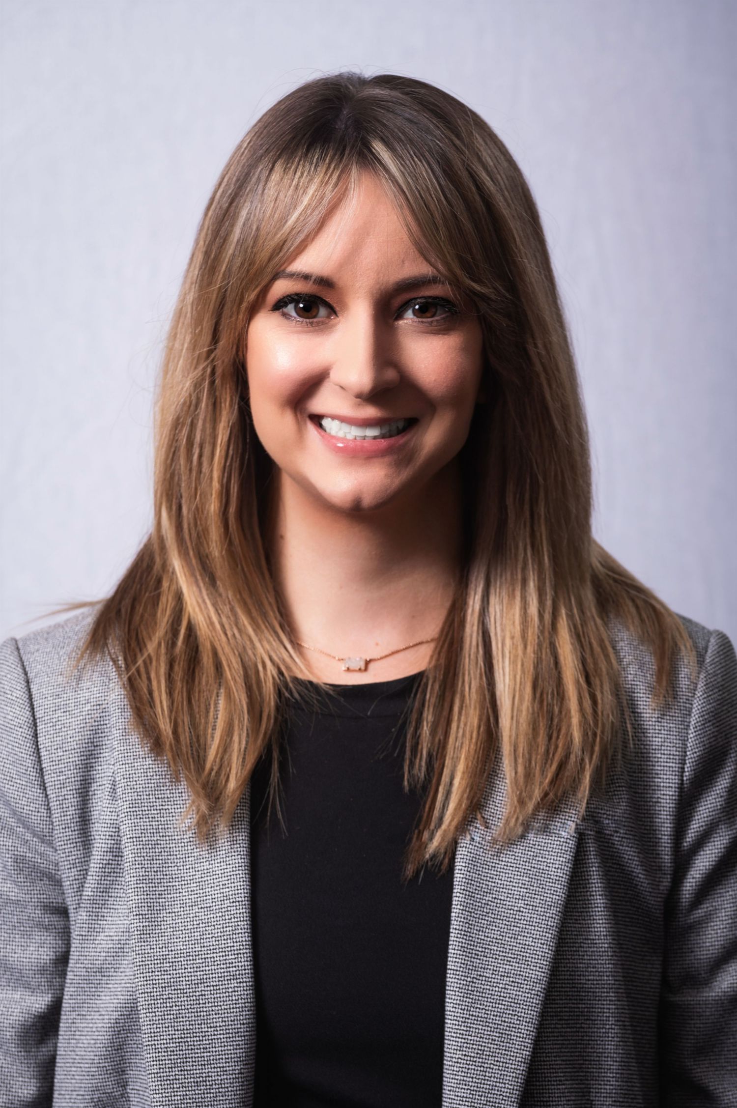 Professional studio portrait of someone in a gray blazer and black top against a neutral background.