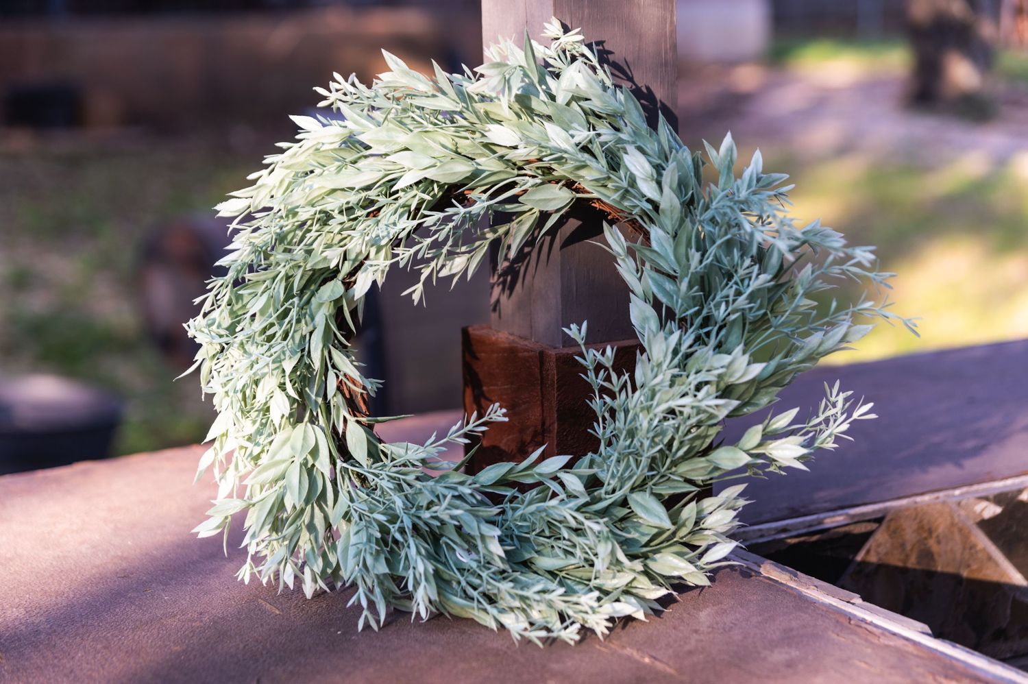 Decorative sage green wreath with dried leaves on wooden surface.
