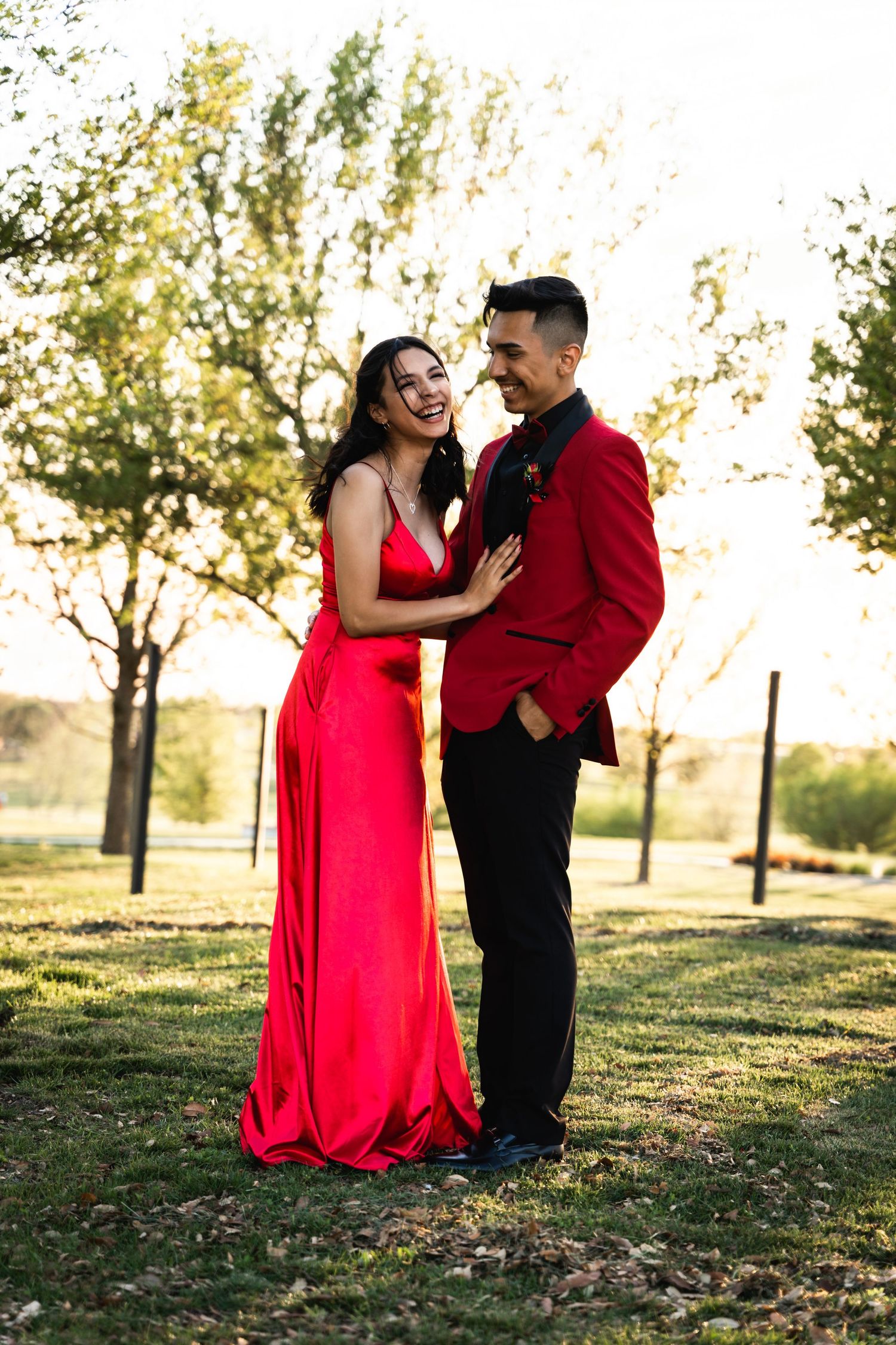 A couple shares a joyful moment together in formal wear against a sunset backdrop.